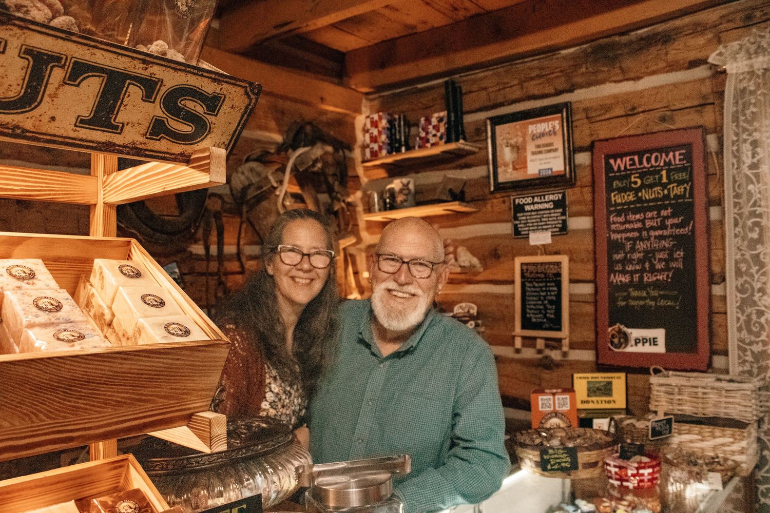 Cheerful older couple posing inside a cozy rustic wooden shop filled with nuts and specialty goods.