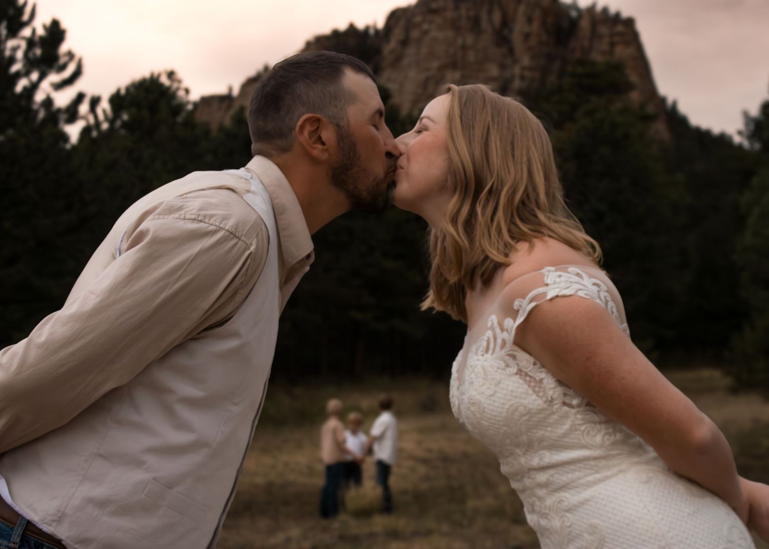 Bride and groom sharing a romantic kiss outdoors with a rocky mountain backdrop at their wedding ceremony.