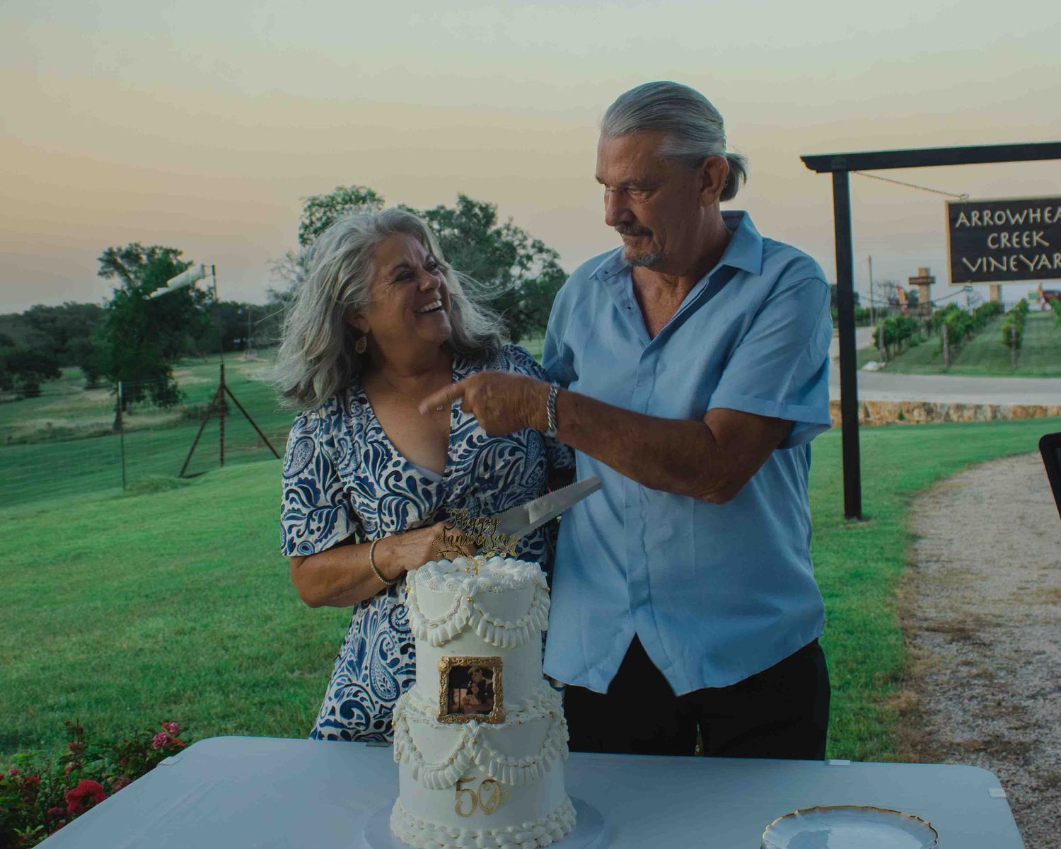 Couple cutting a wedding anniversary cake outdoors at Arrowhead Creek Vineyard at sunset.