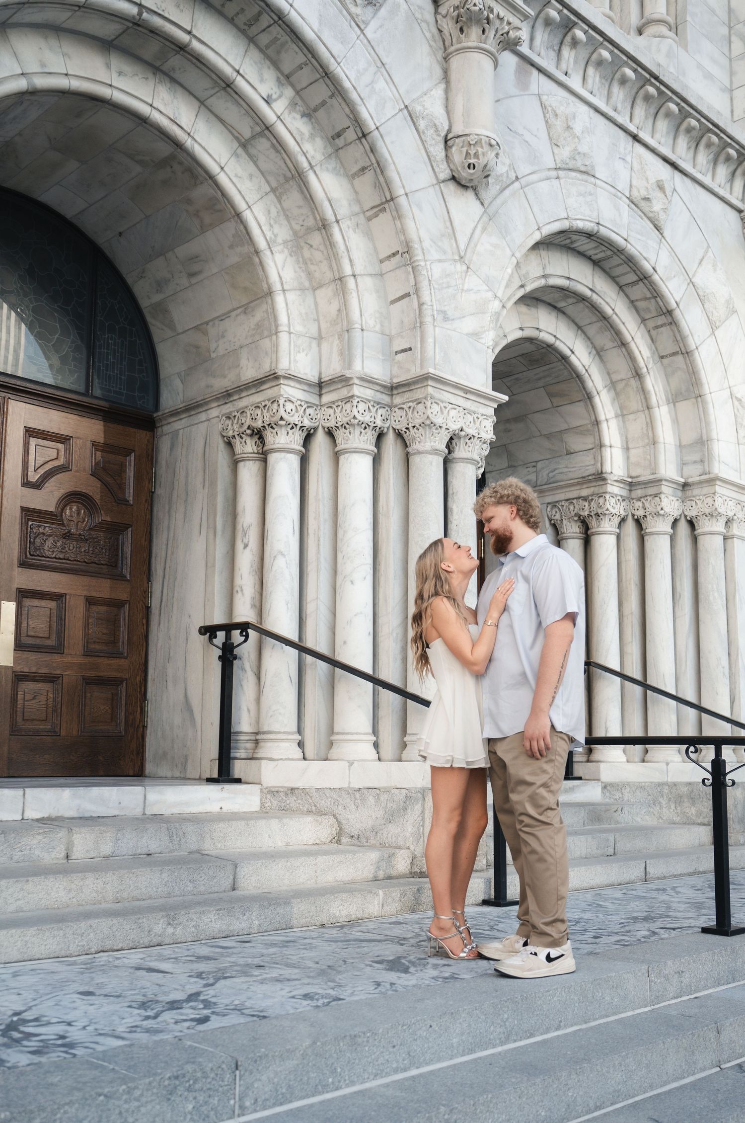 Couple sharing a romantic moment on the steps of a grand marble cathedral with ornate arches.