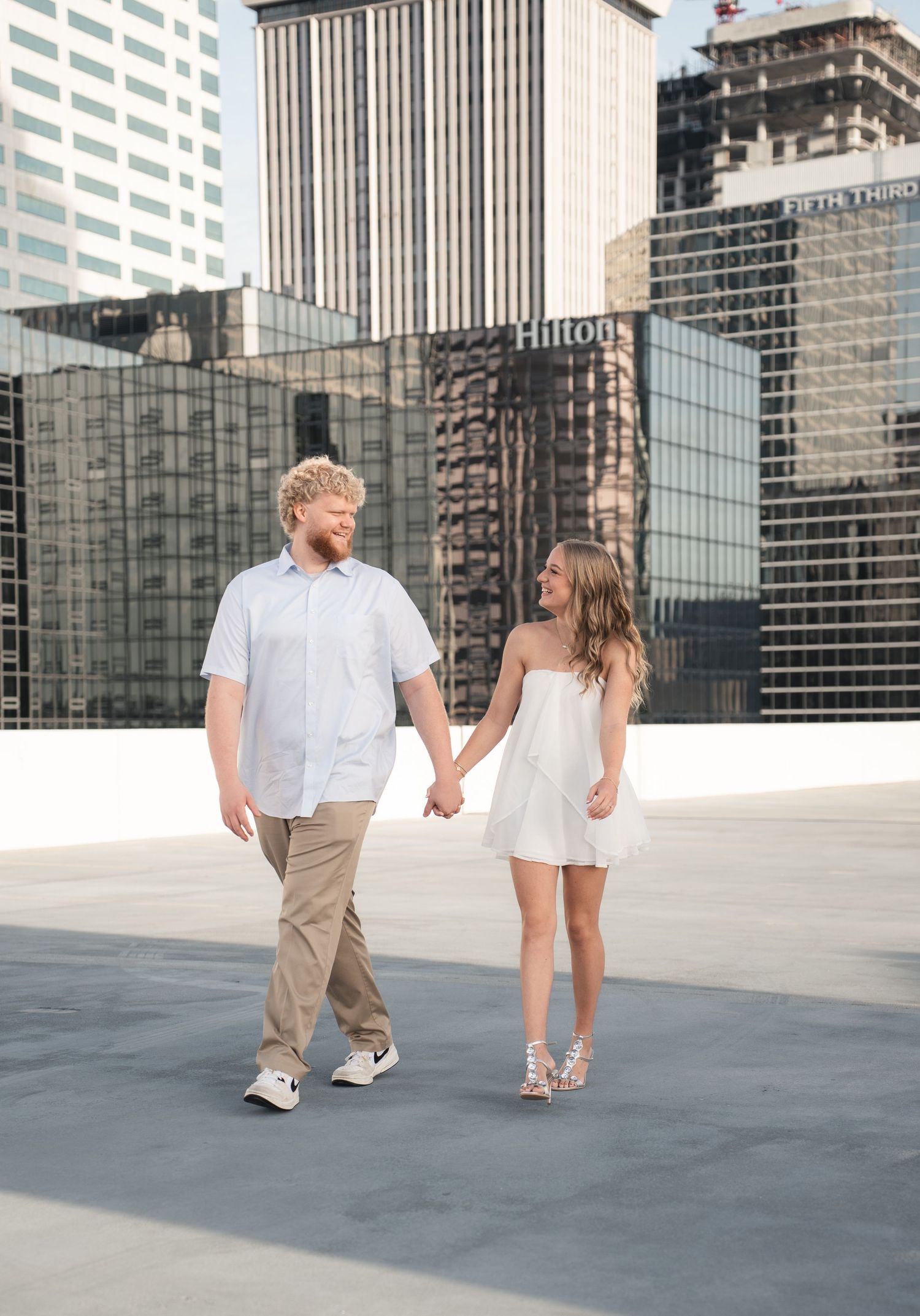 Couple holding hands walking on rooftop with Hilton hotel and city skyline in background.