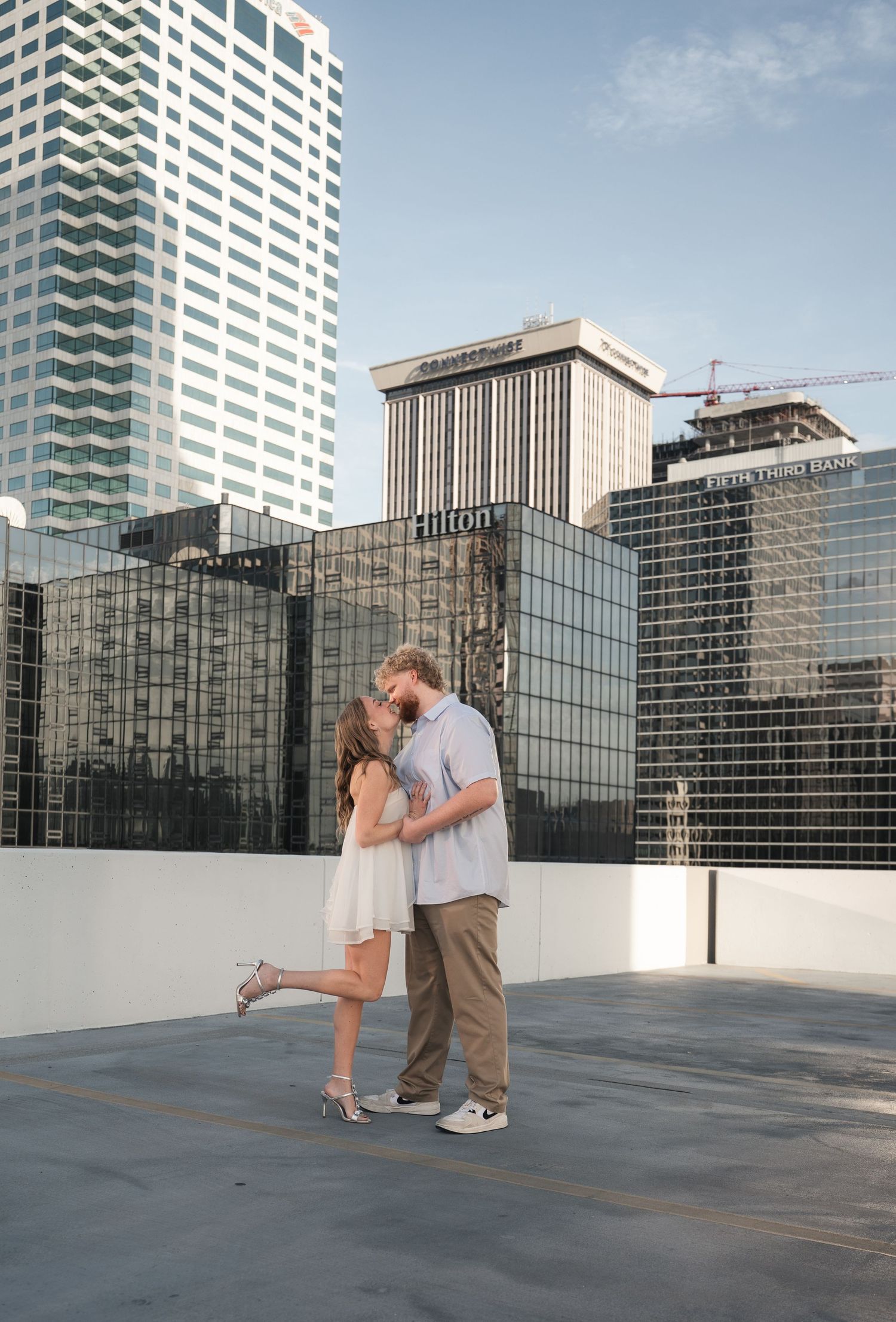 Couple sharing a romantic kiss on a rooftop with city skyline and Hilton hotel in the background.
