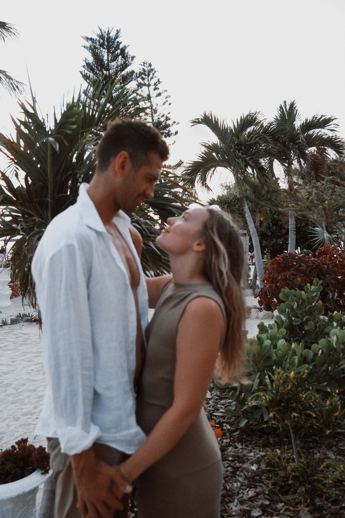 Couple holding hands and gazing at each other in a tropical garden with palm trees.