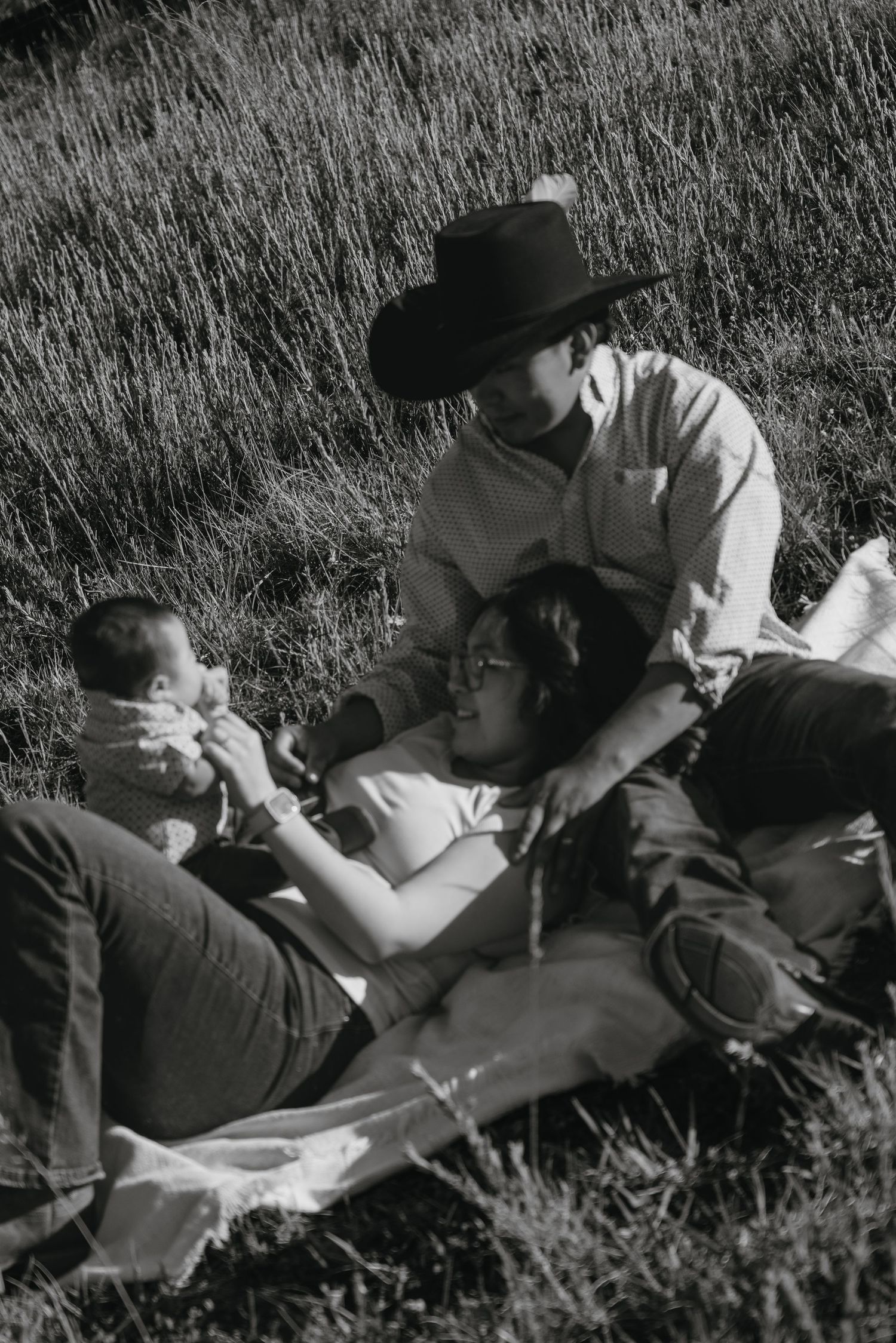 Black and white photo of a family relaxing in a grassy field, with father in cowboy hat and baby.