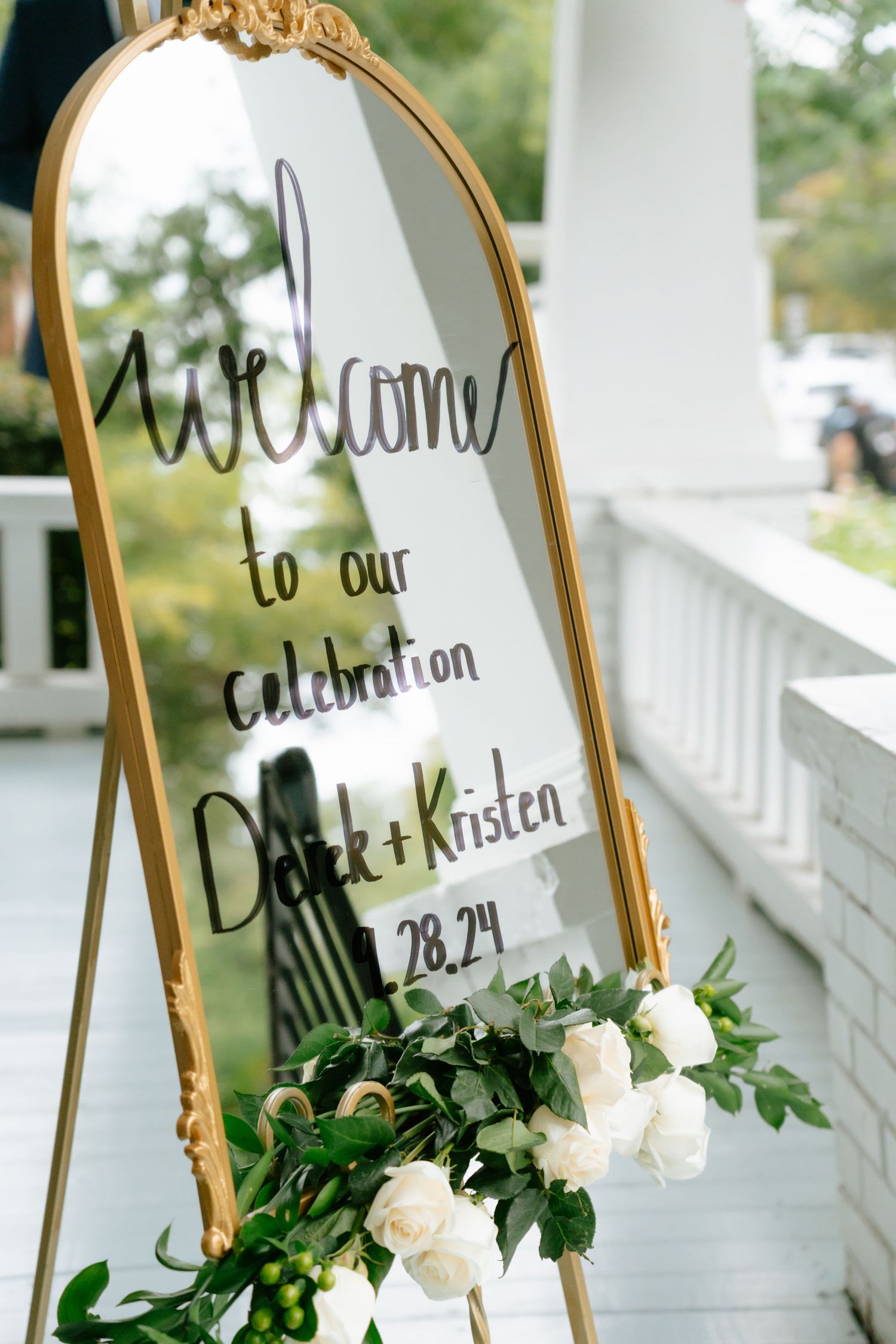 Gold arched mirror wedding welcome sign for Derek and Kristen decorated with white roses and greenery.