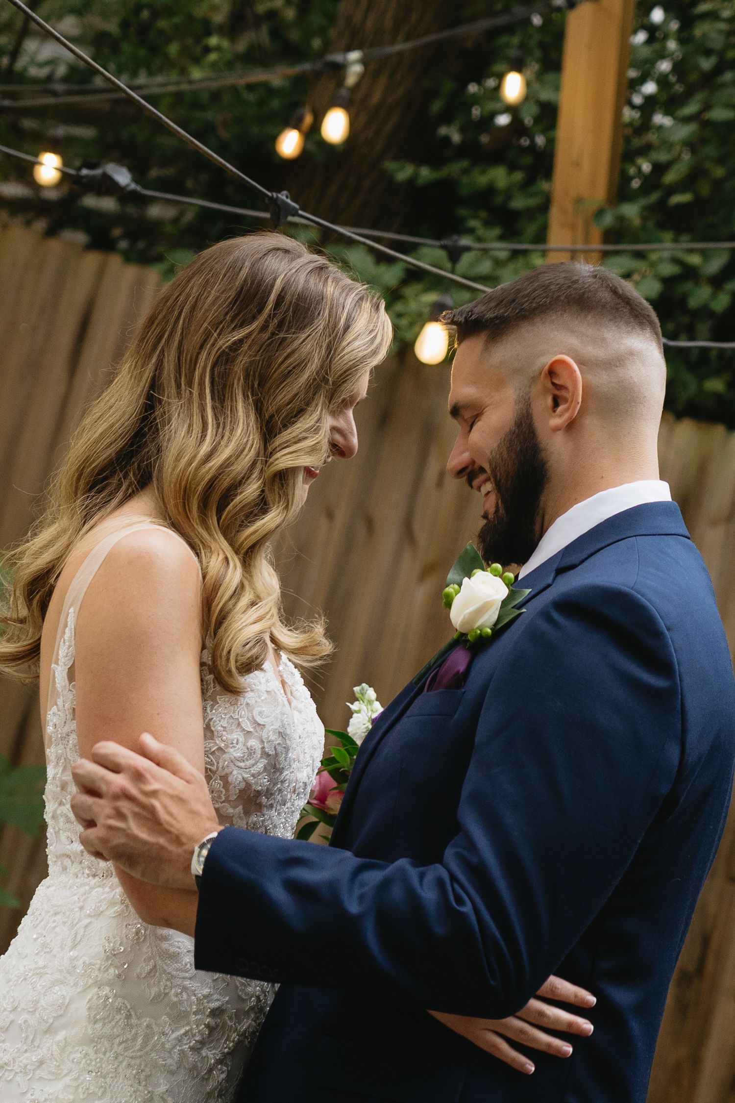 Bride and groom share a romantic moment outdoors, smiling at each other under string lights at their wedding.