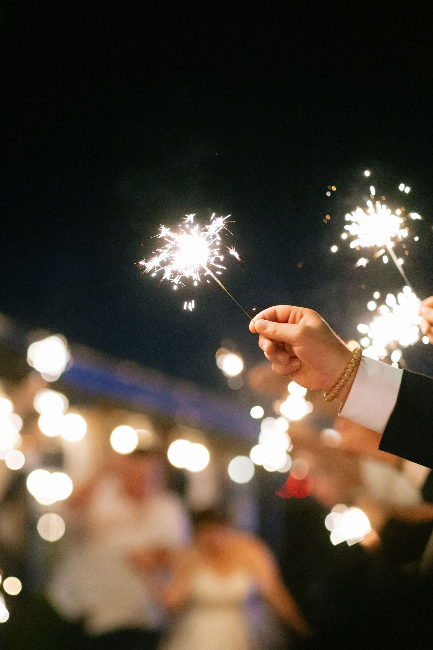 A hand holds a bright sparkler against a dark night sky at an outdoor wedding celebration.