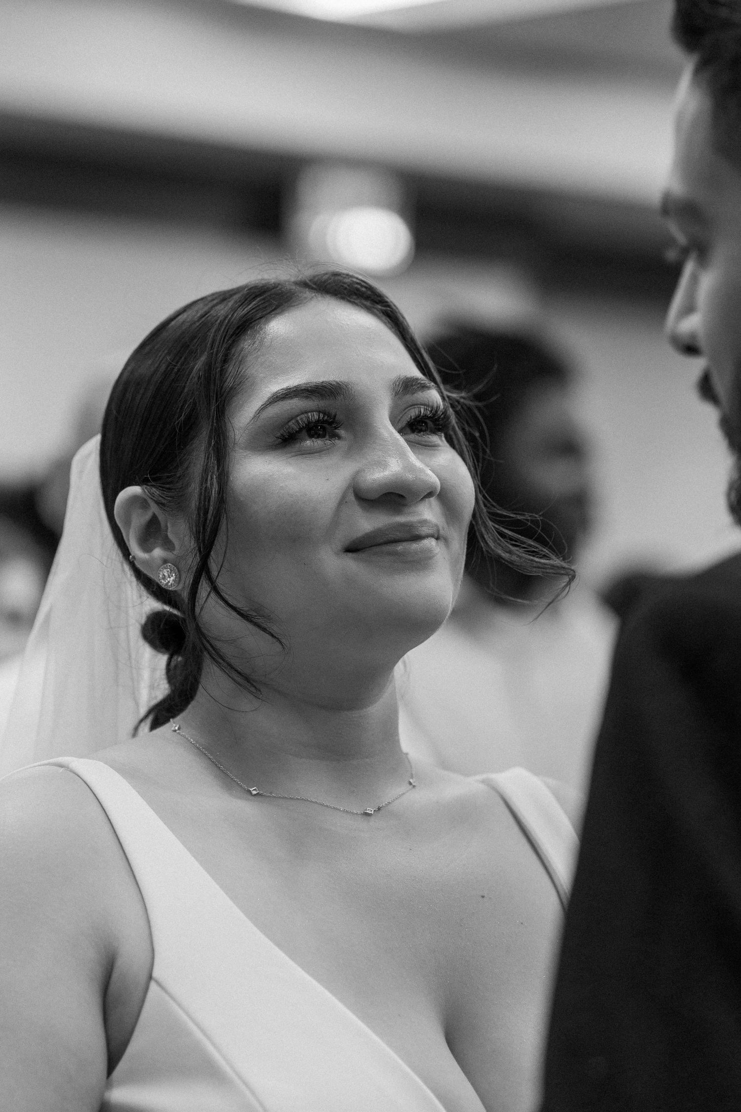 A radiant bride in a white dress and veil gazes lovingly at her groom in a black and white photo.