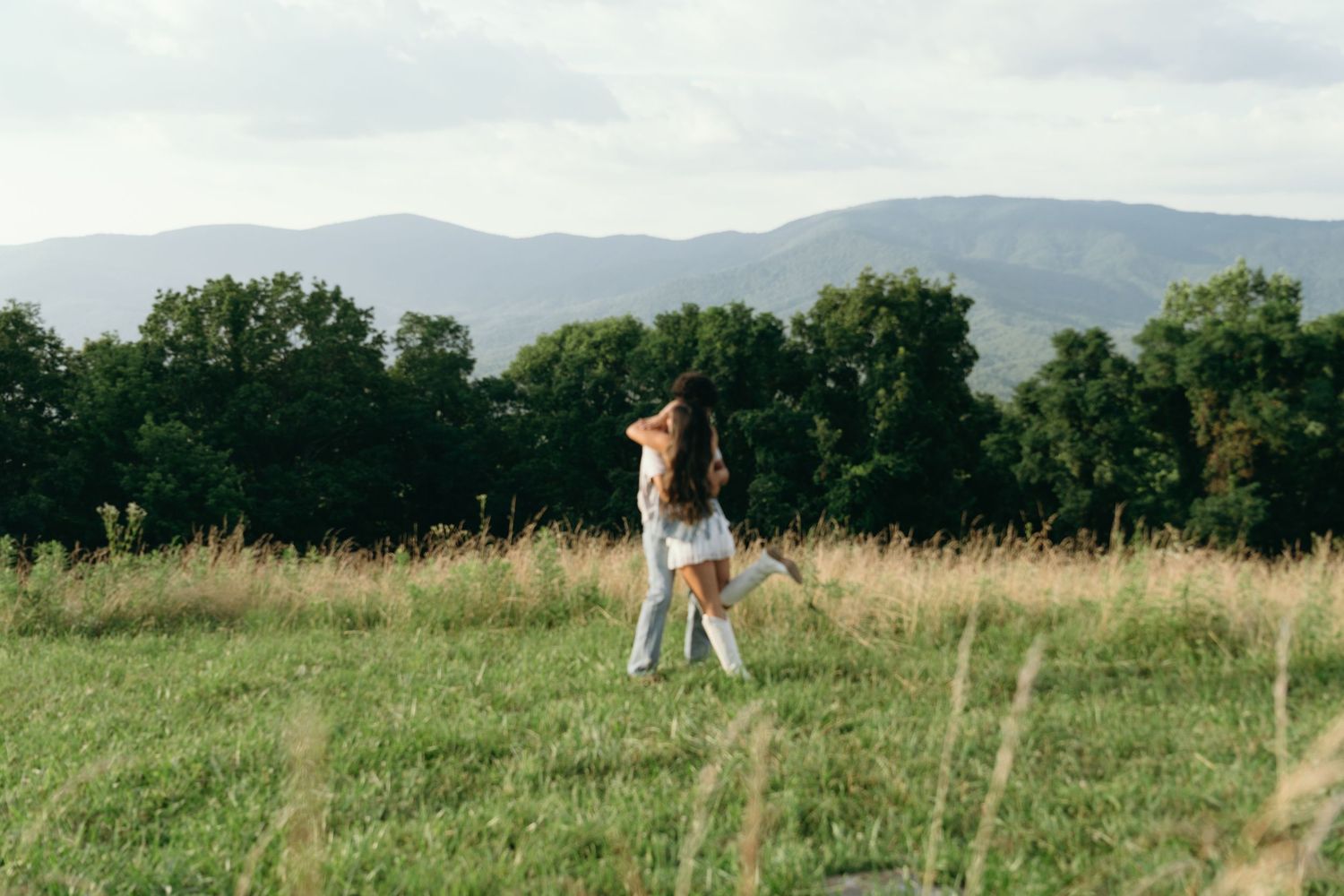 Couple dancing in a lush green meadow with mountains and trees in the background.