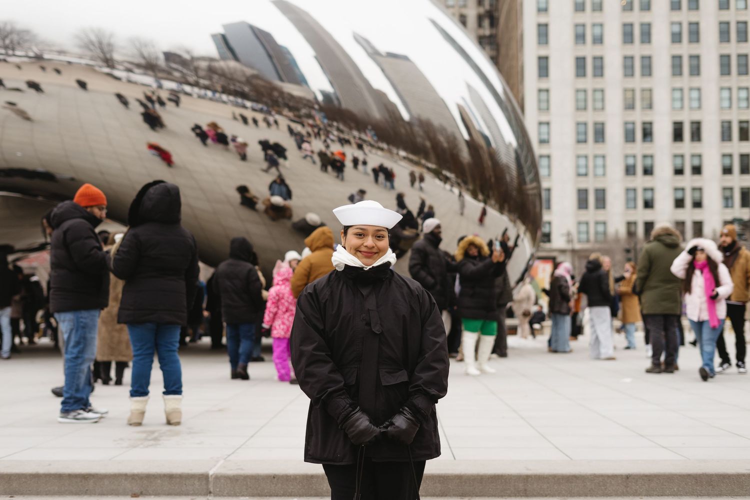 Woman in black coat smiling in front of the Cloud Gate sculpture in Chicago's Millennium Park.