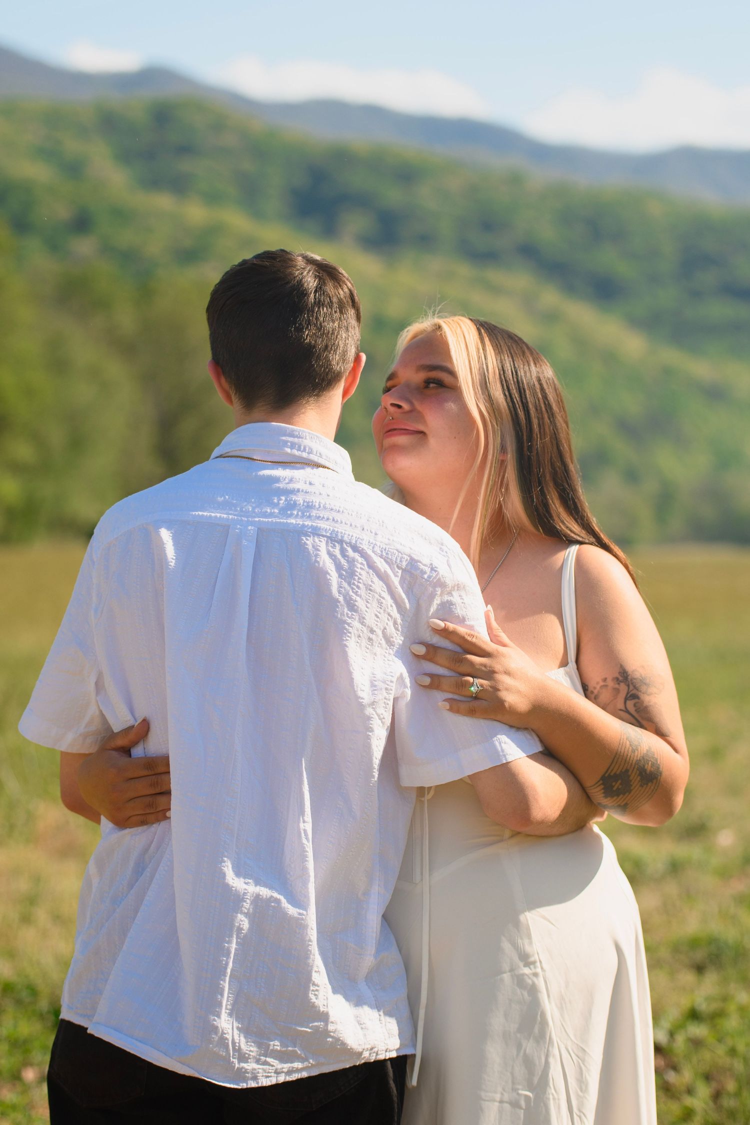 Couple embracing and smiling at each other in a scenic mountain meadow on a sunny day.