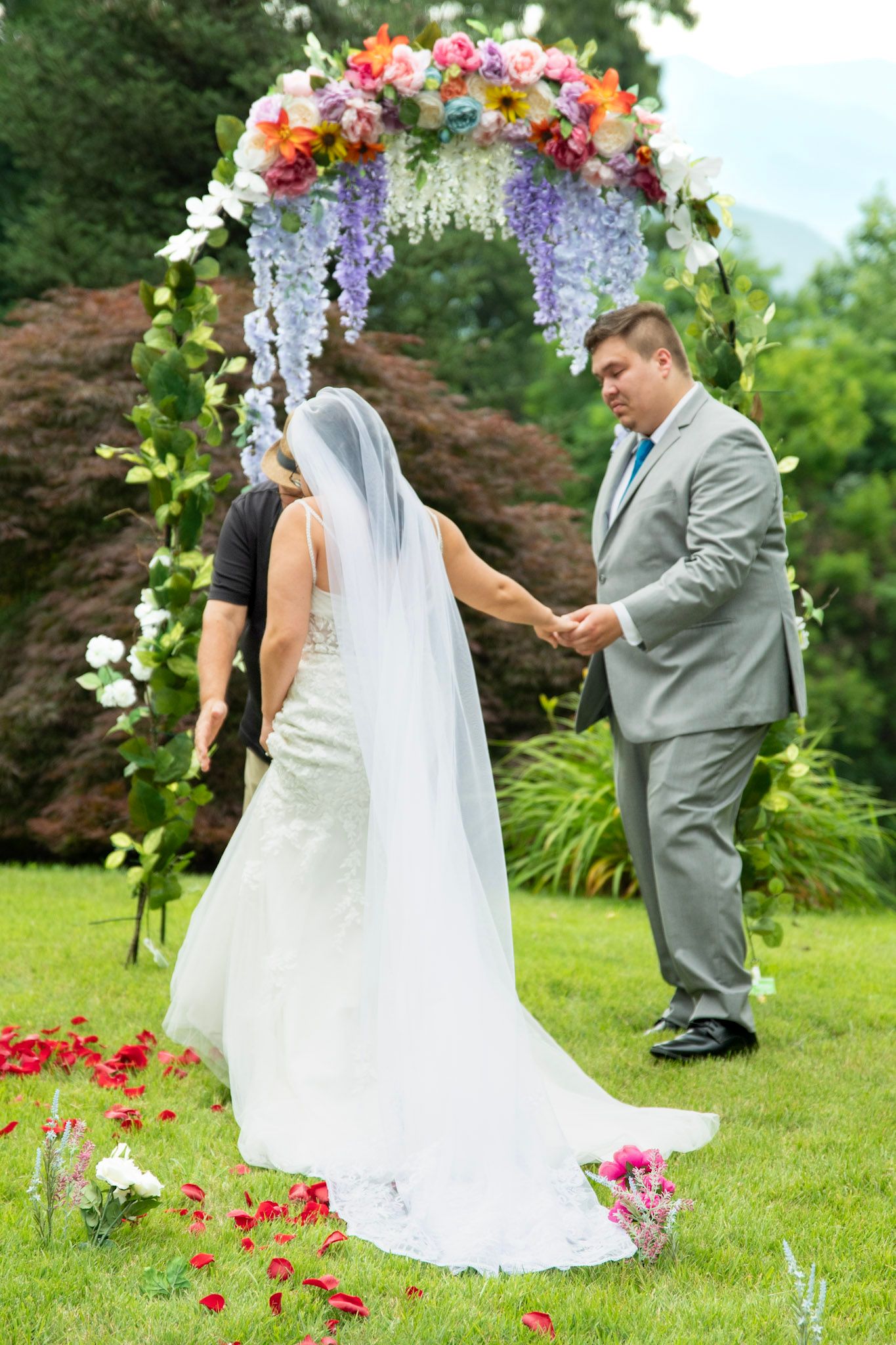 Bride and groom holding hands under a colorful floral arch during an outdoor wedding ceremony.