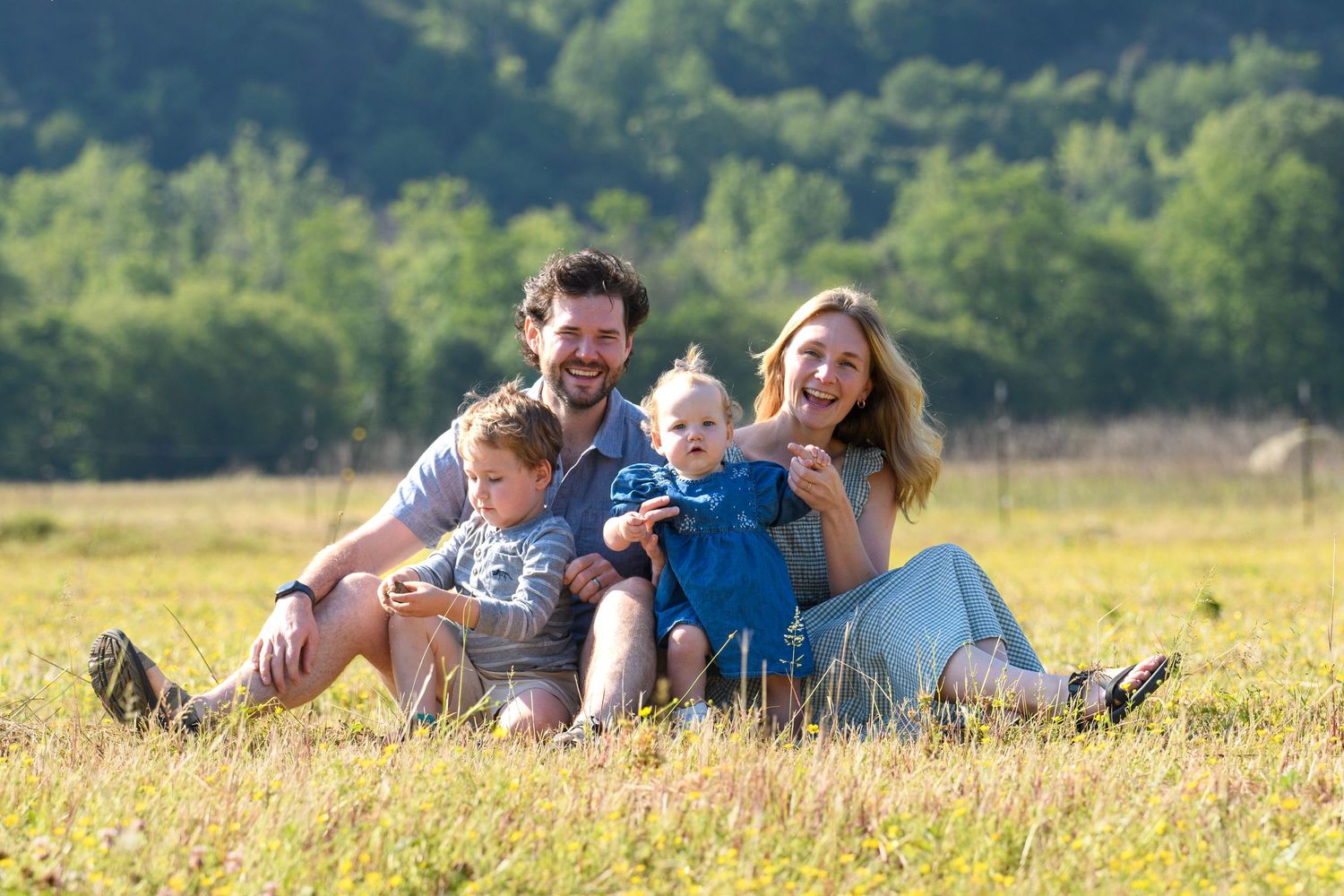 Joyful family of four sitting together in a golden sunlit field smiling at camera.