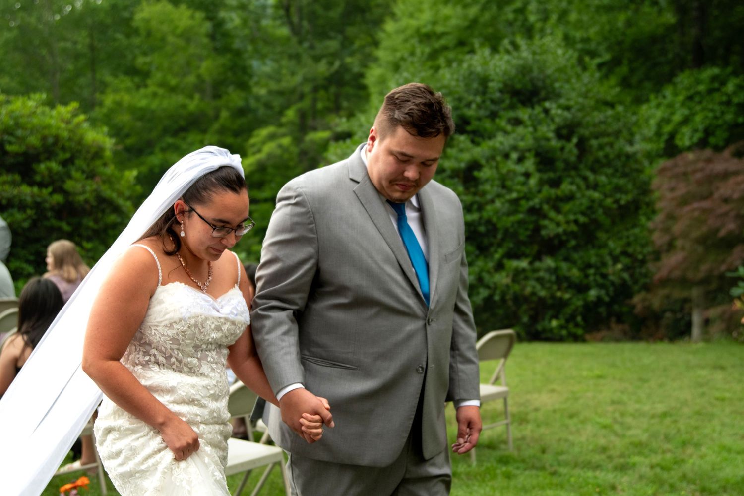 Bride and groom walking hand in hand during outdoor wedding ceremony in green garden.