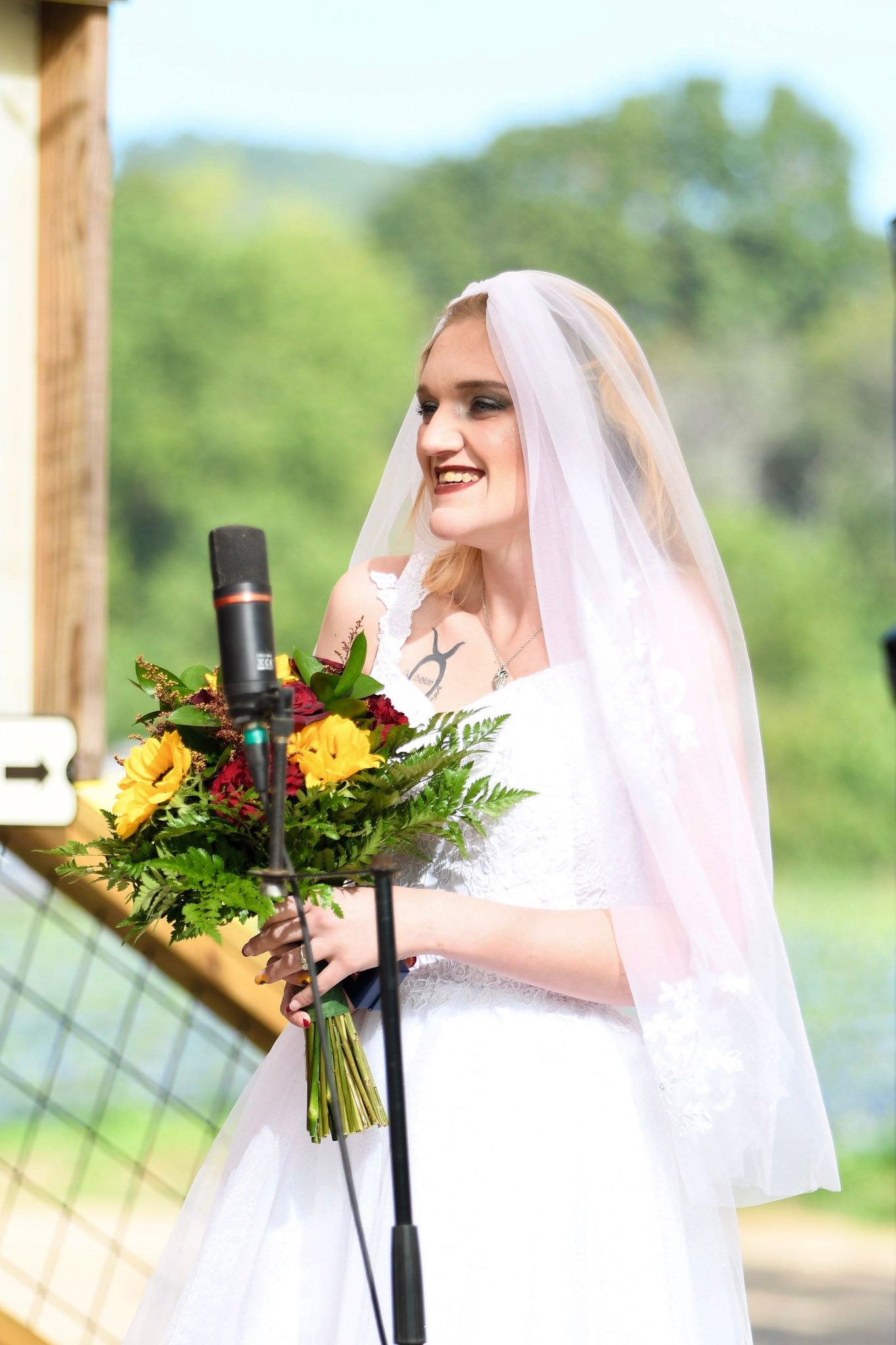 Smiling bride in white wedding gown and veil holding colorful bouquet of yellow and red flowers.