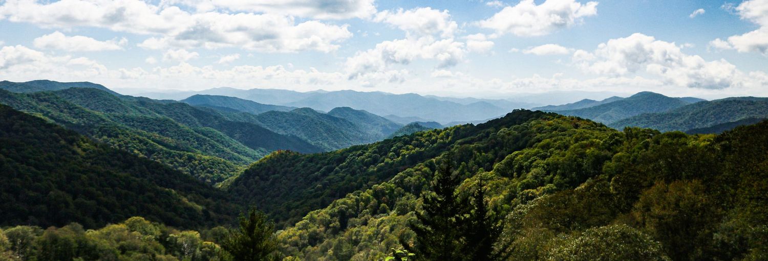 Panoramic view of lush green Smoky Mountains under a partly cloudy blue sky.