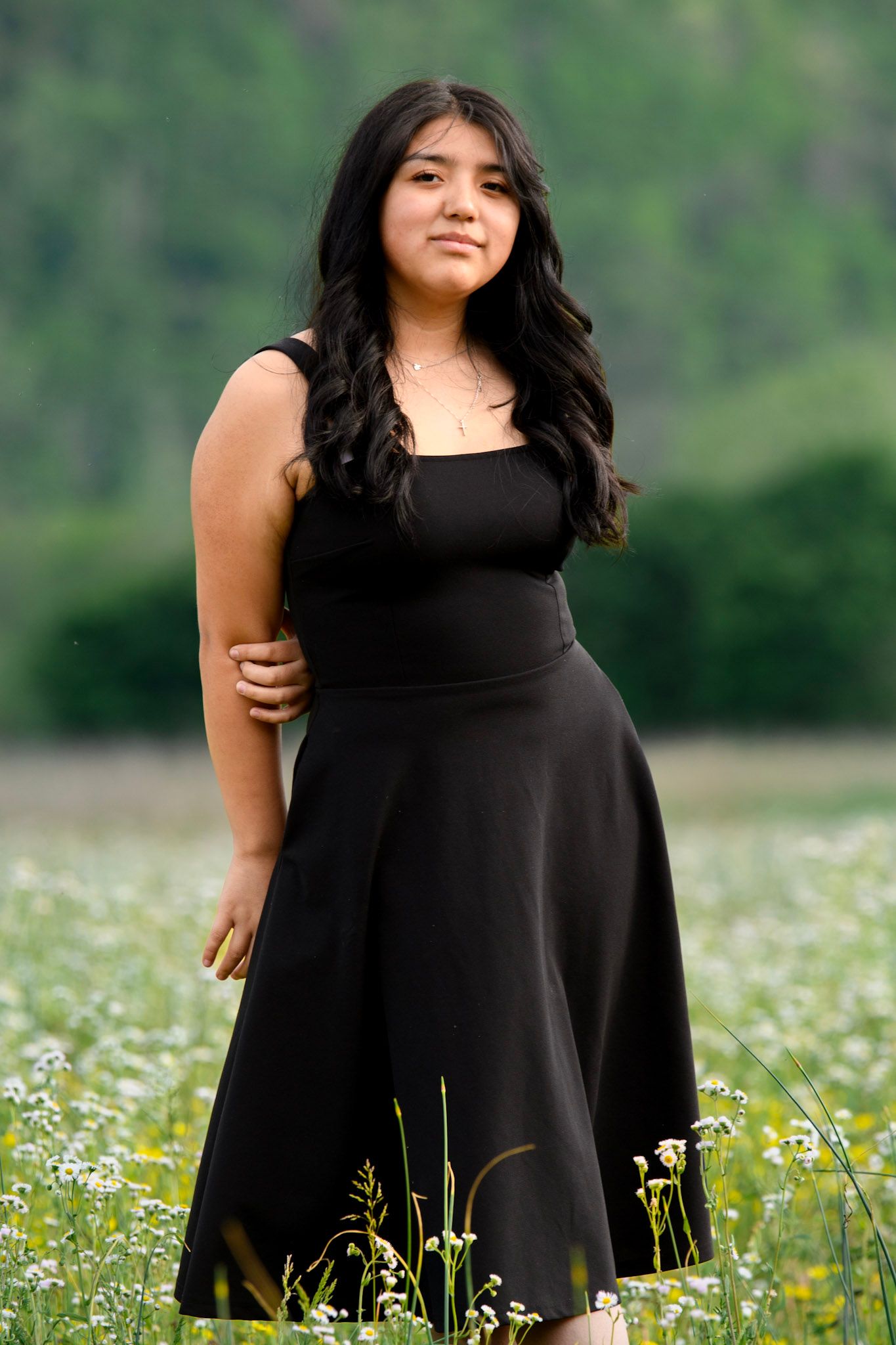 Young woman in black dress standing in a wildflower field with green hills in the background.