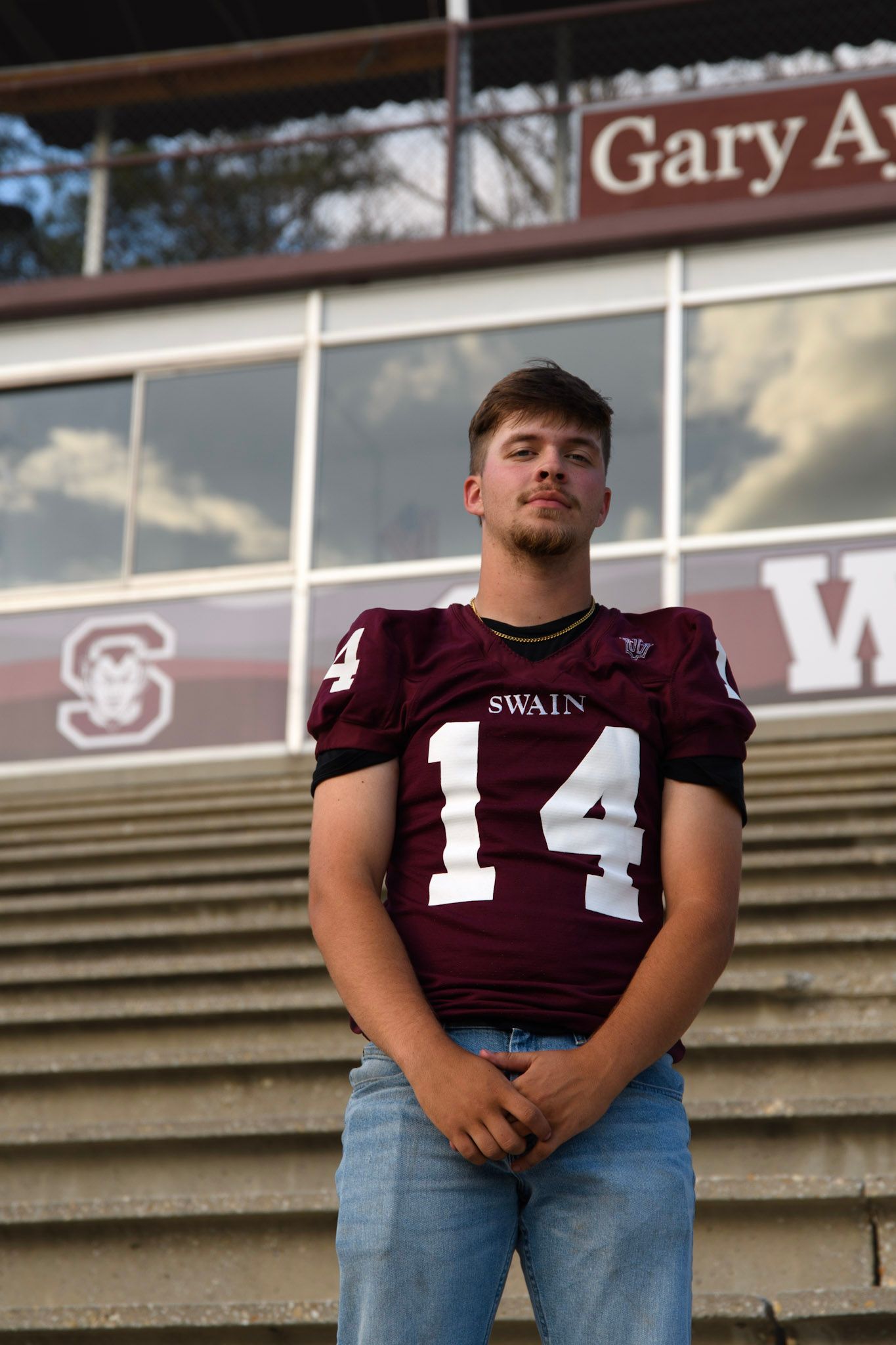 Male athlete in Swain number 14 maroon football jersey standing in stadium bleachers.