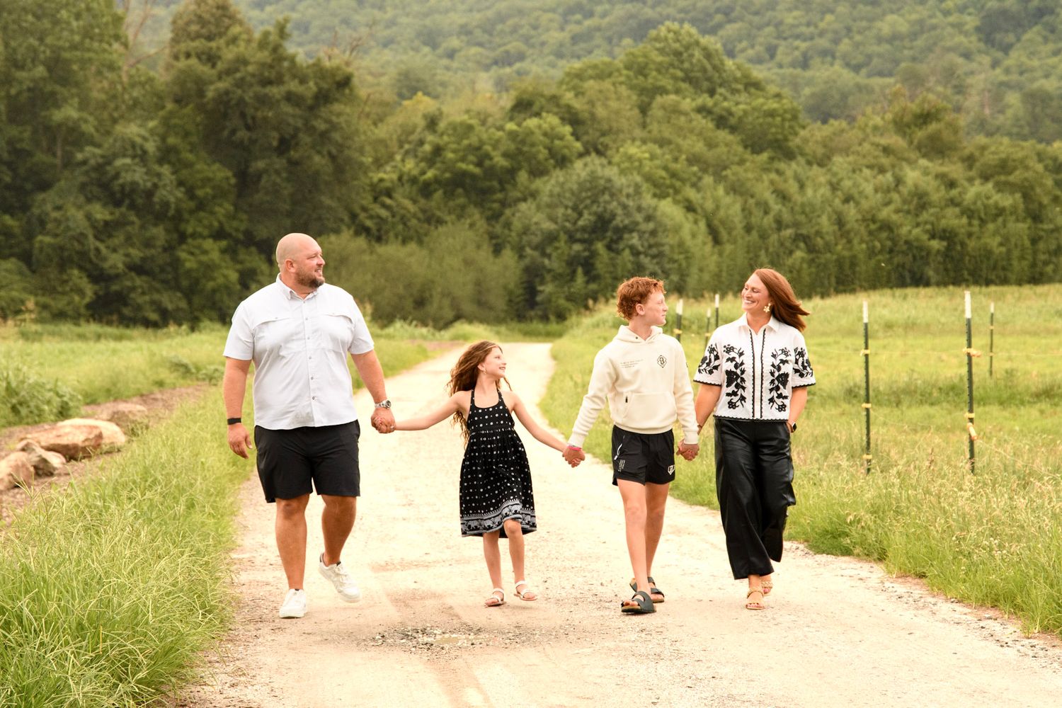 Happy family of four walking hand in hand down a scenic rural dirt road.