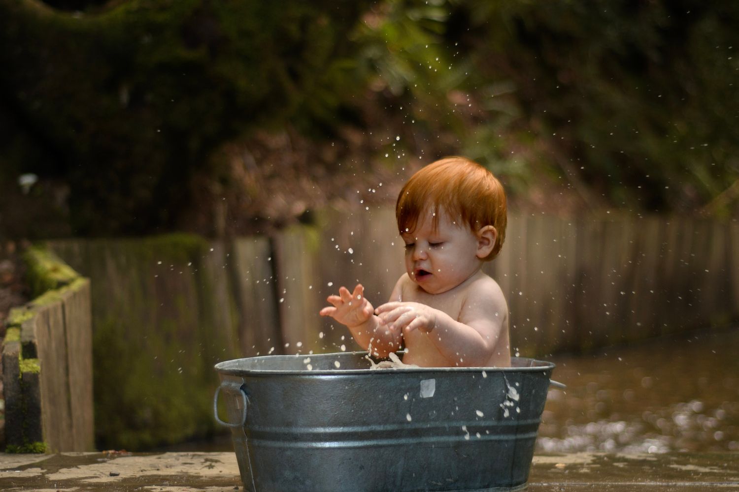 Redhead toddler splashing and playing in a metal tub outdoors.