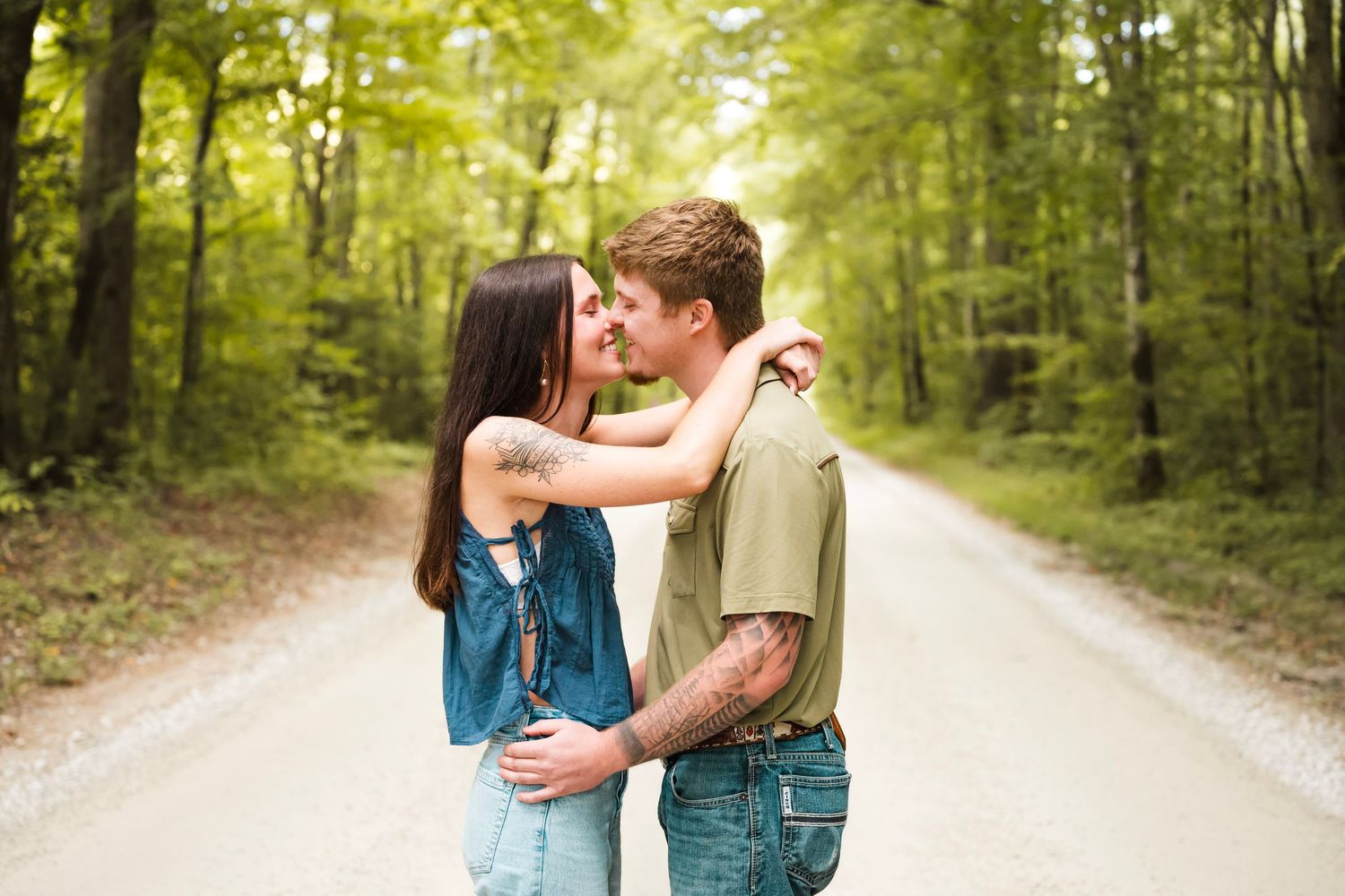 Couple sharing a romantic moment on a tree-lined dirt road, about to kiss outdoors.