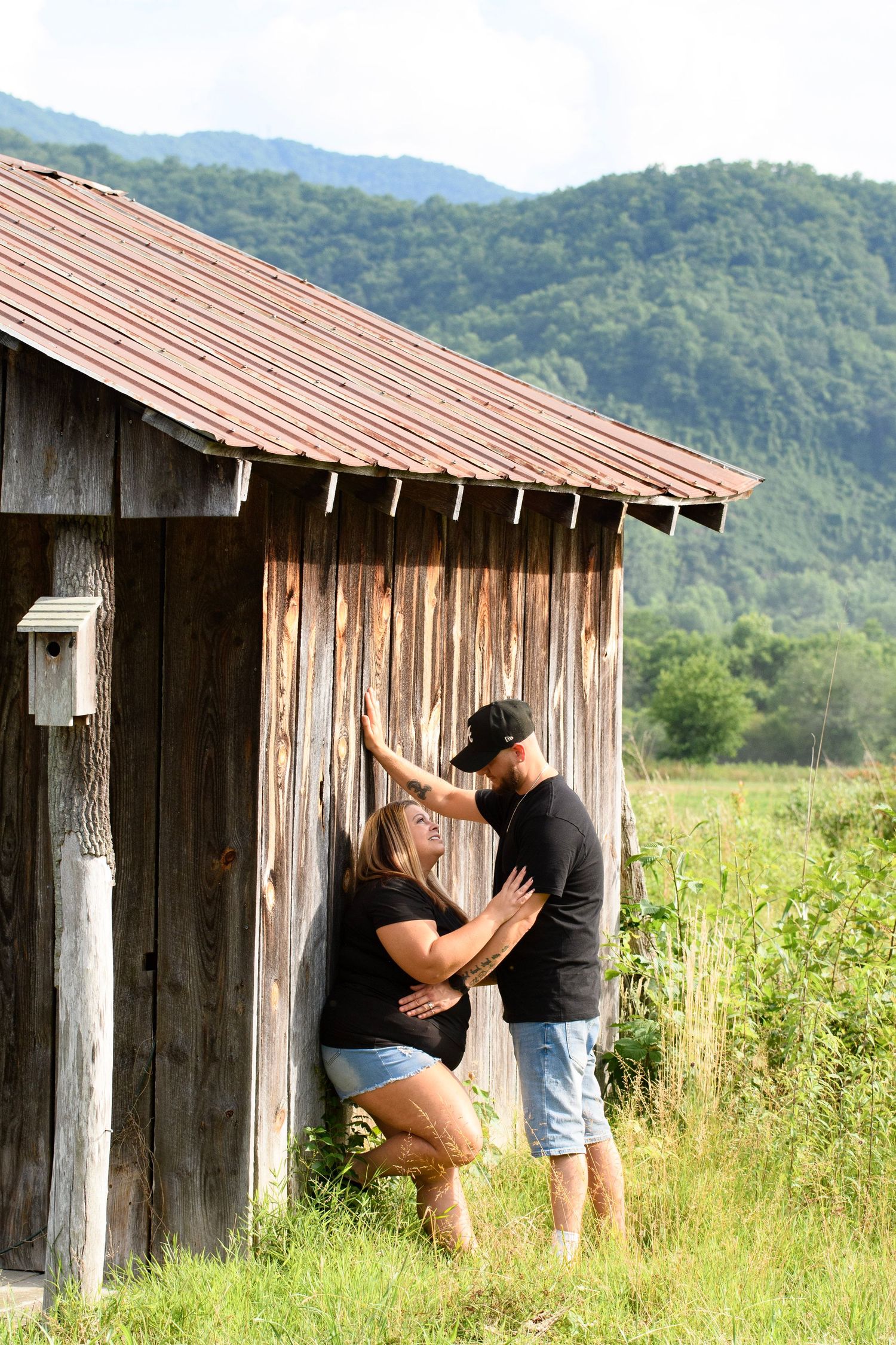 Couple sharing a romantic moment leaning against a rustic wooden barn with mountain views.