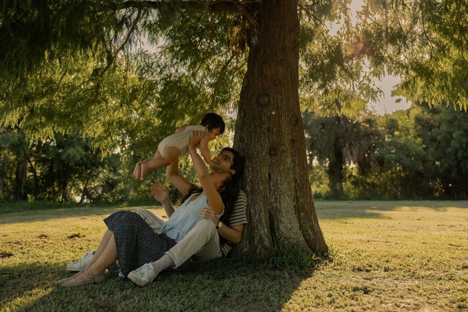 Man and woman sitting under the shade of a tree playing with their baby