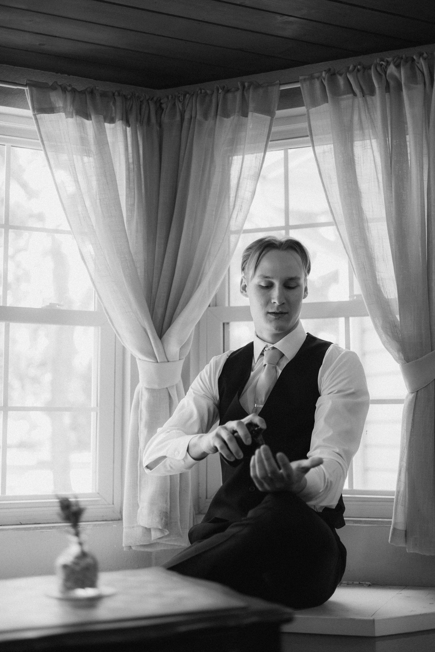 A black and white image of a man in dress clothes spraying cologne on his wrist.