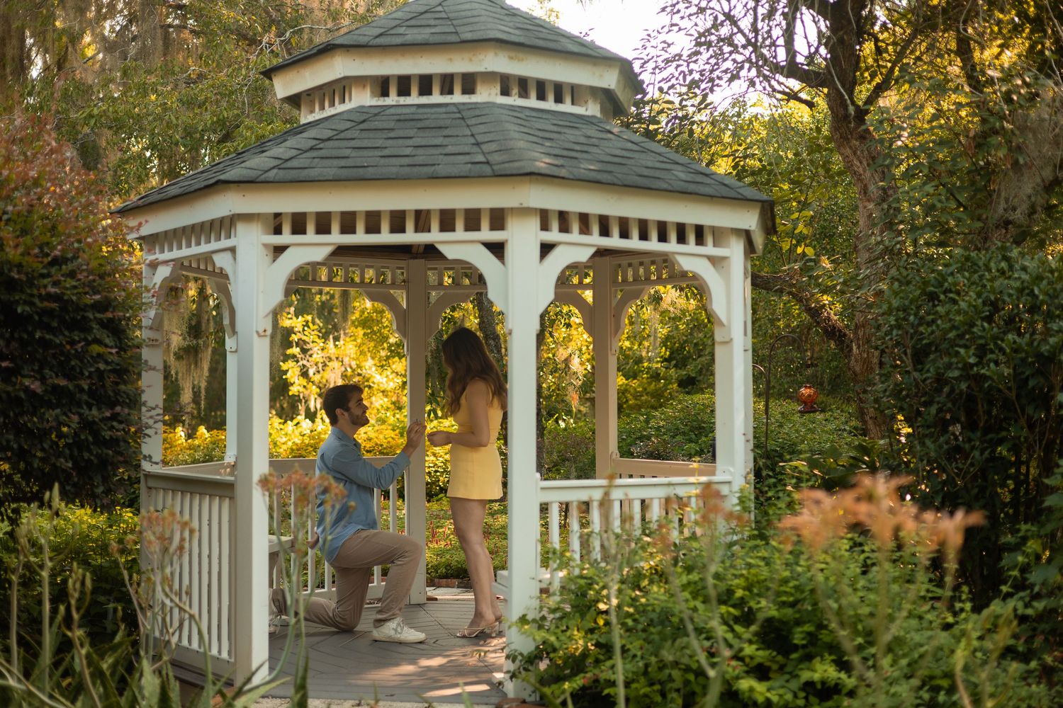 A man on one knee proposing to a woman in a white gazebo