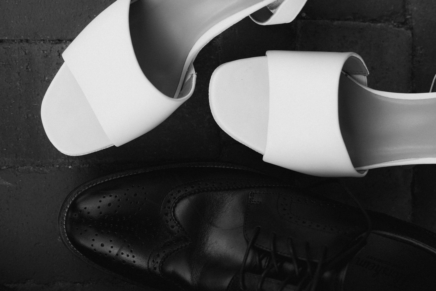Black and white image of white heels and black men's dress shoes.