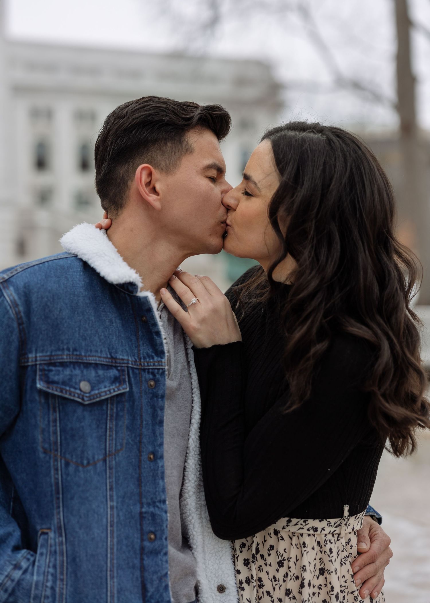 Close-up of a couple sharing a tender kiss outdoors, woman wearing a diamond engagement ring.