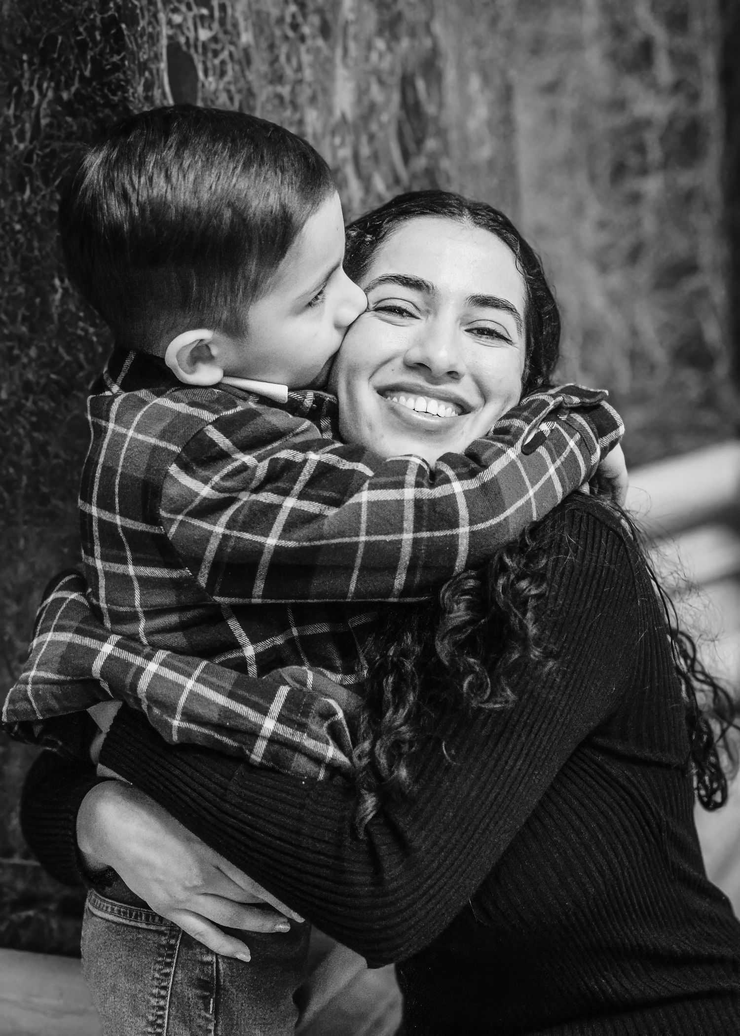 Joyful black and white portrait of smiling woman being hugged and kissed by young boy.