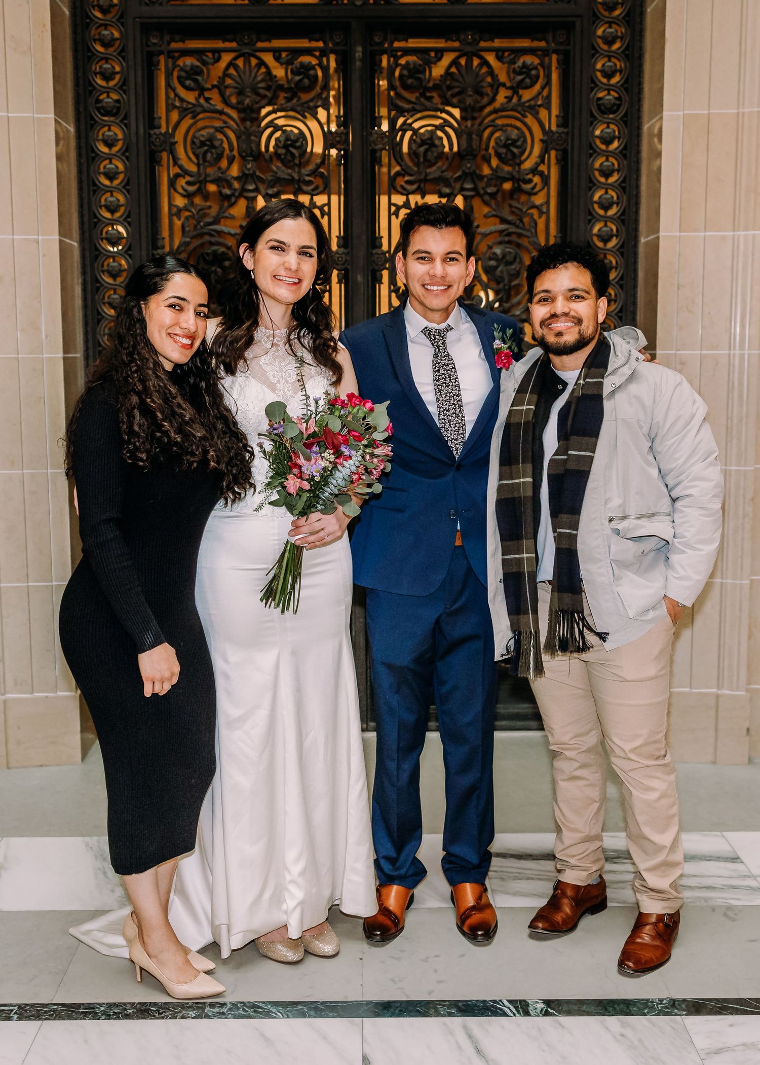 Bride and groom pose with two wedding guests in front of ornate golden doors at a city hall wedding.
