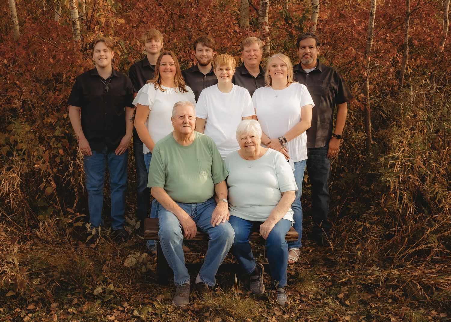 Large multigenerational family group portrait outdoors with vibrant red autumn foliage background.