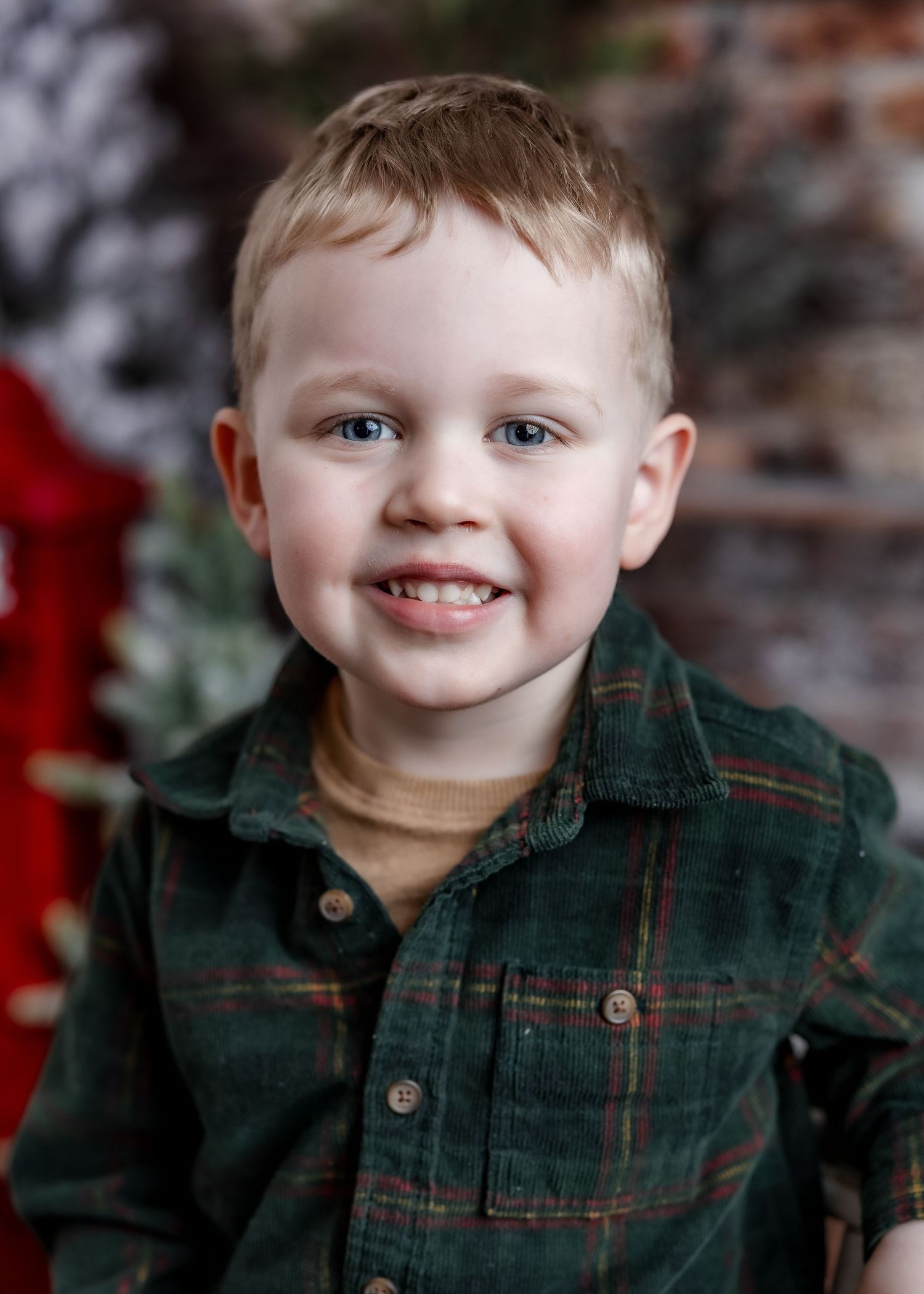 Smiling young boy with blue eyes wearing green plaid shirt in Christmas photo session.