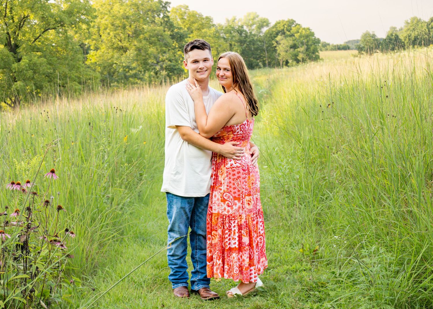 Young couple embracing on a grassy path, woman wearing a coral floral maxi dress.