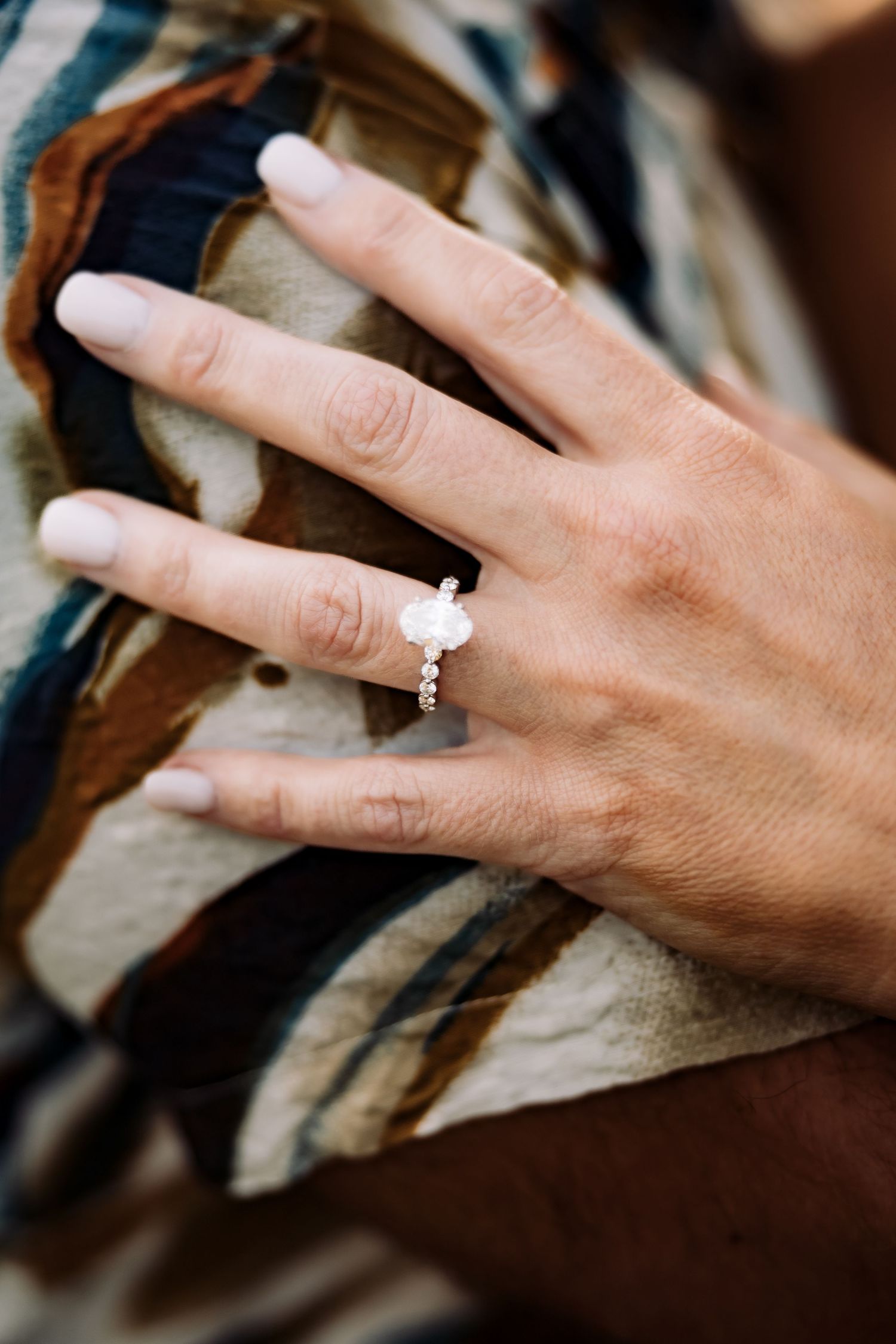 Close-up of a womans hand wearing an elegant oval diamond engagement ring on a rose gold band.