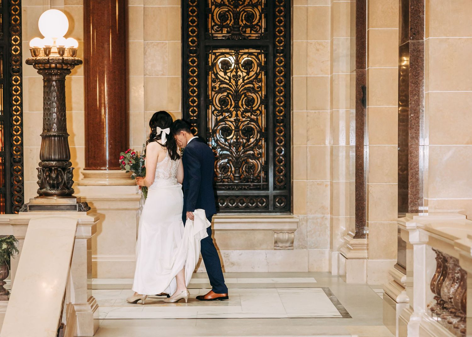 Bride and groom share intimate moment near ornate golden door on marble steps.