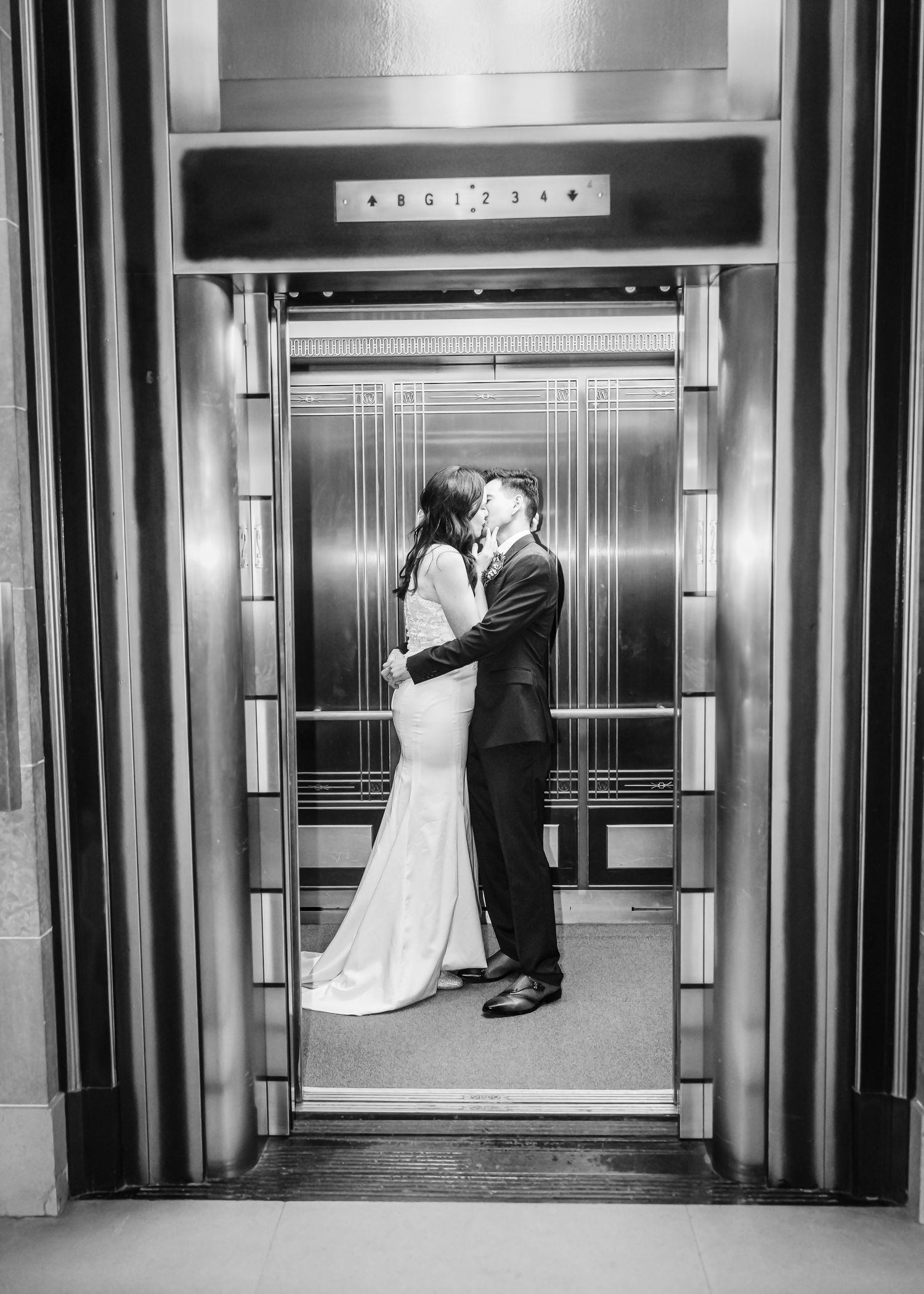 Black and white photo of bride and groom sharing a kiss inside an elegant Art Deco elevator.