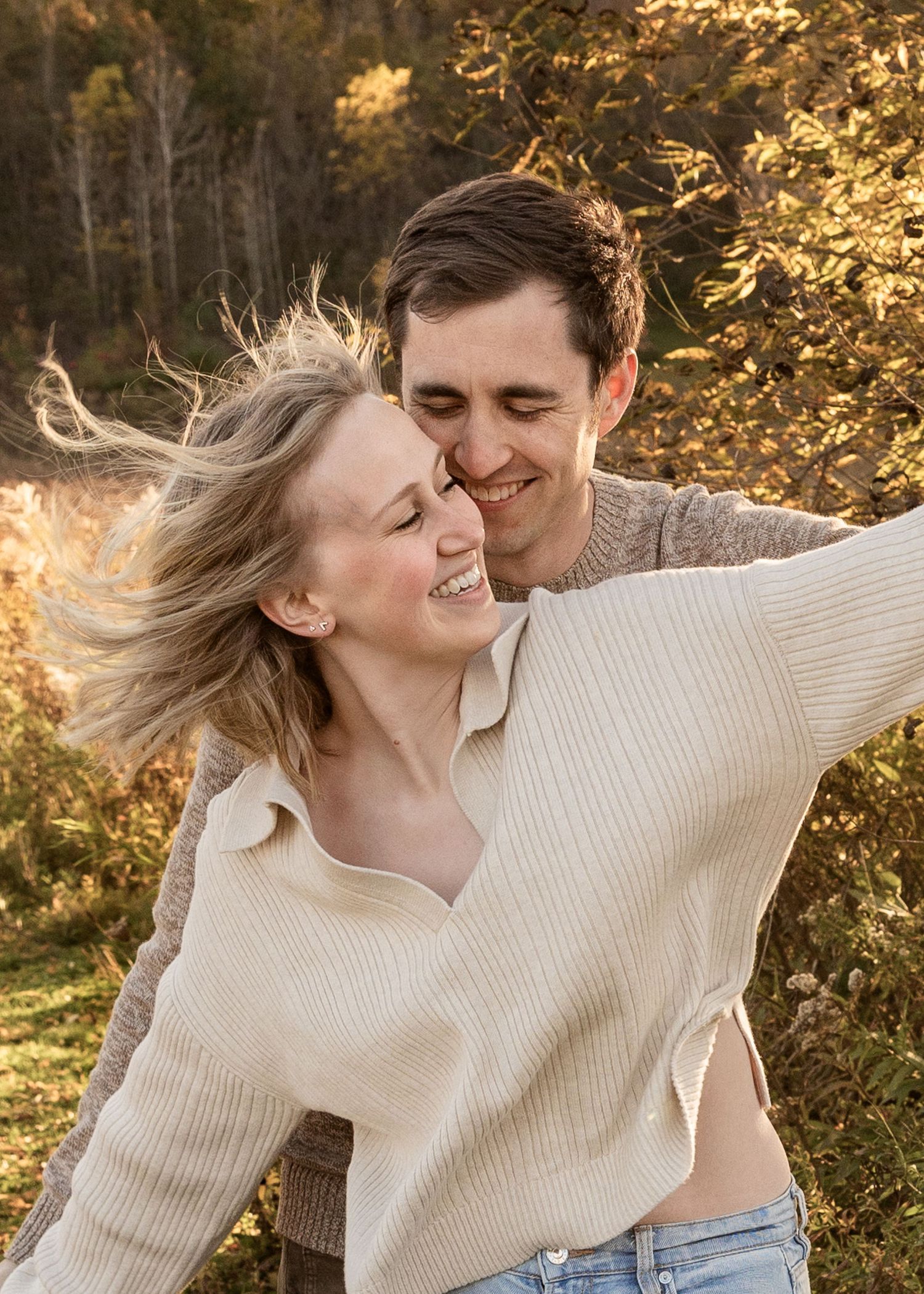 Happy couple embracing outdoors with golden autumn leaves in sunlit nature setting.
