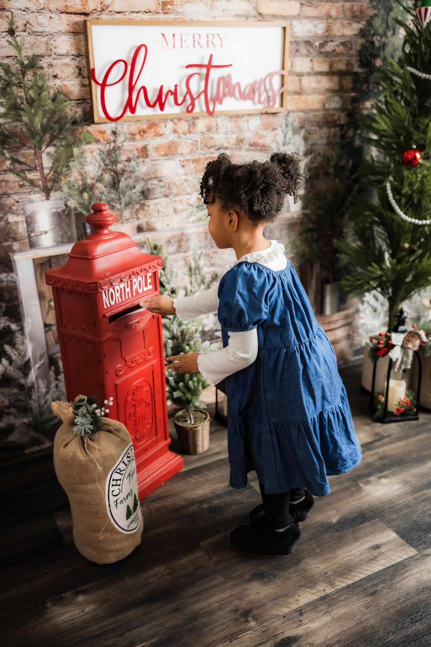 Young girl in blue dress mails letter to North Pole mailbox in Christmas decorated setting.