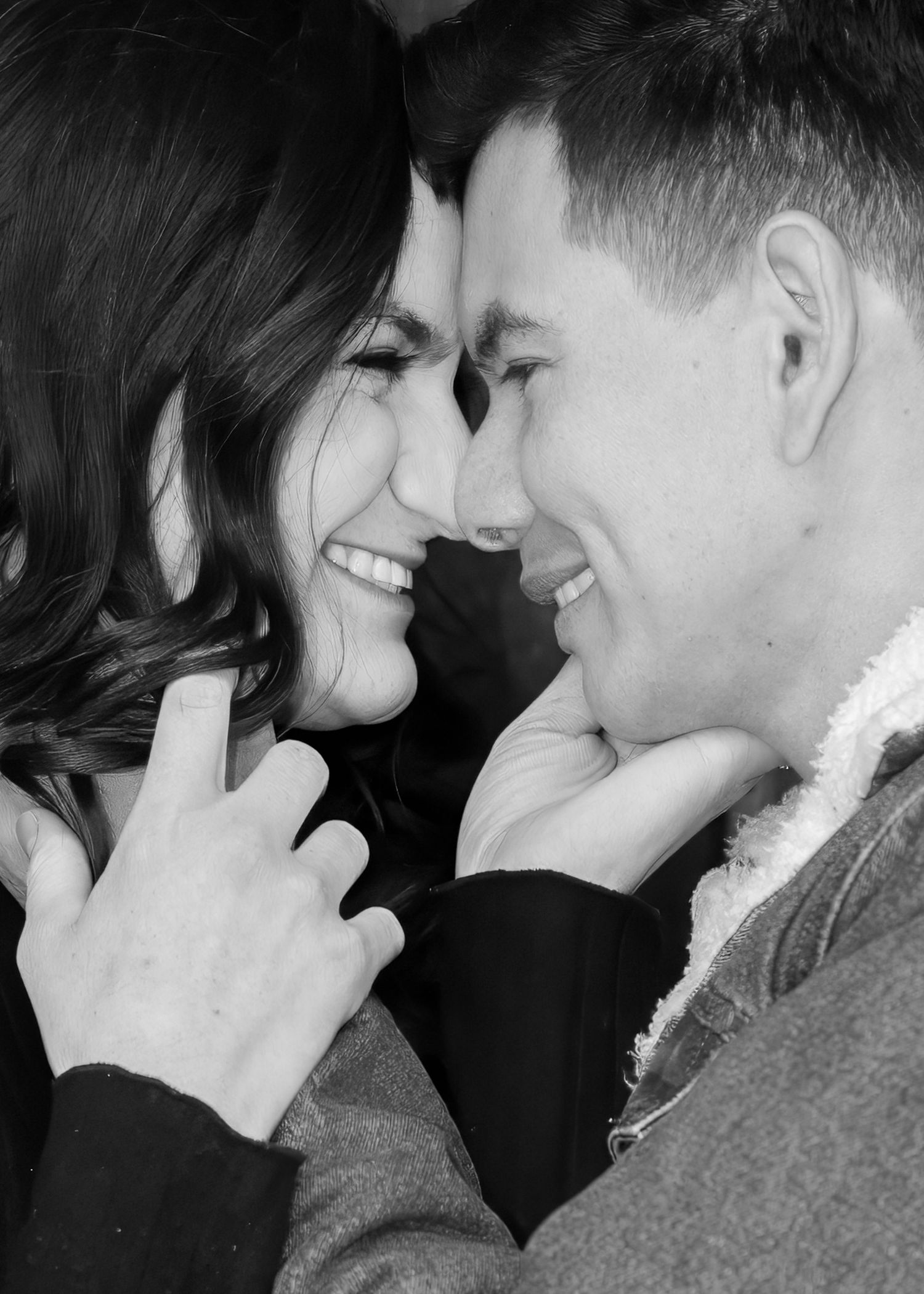A black and white close-up of a joyful couple smiling and touching foreheads in an intimate moment.
