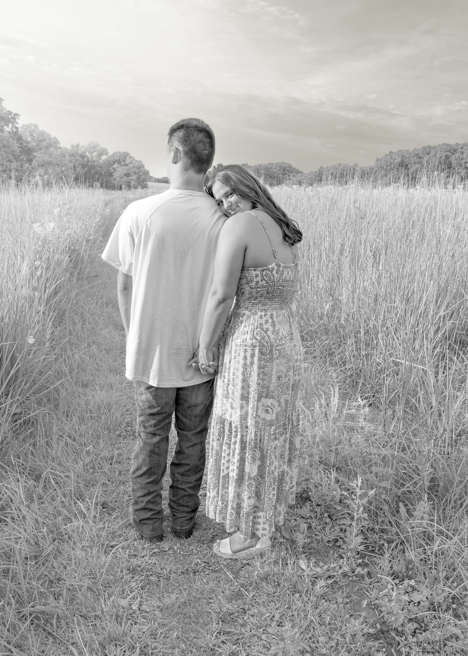 Black and white photo of couple holding hands while standing in a scenic grassy field.