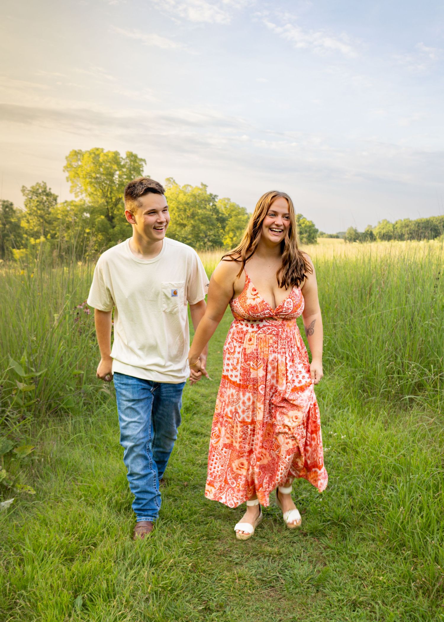 Happy couple holding hands and laughing while walking through a sunny green meadow.