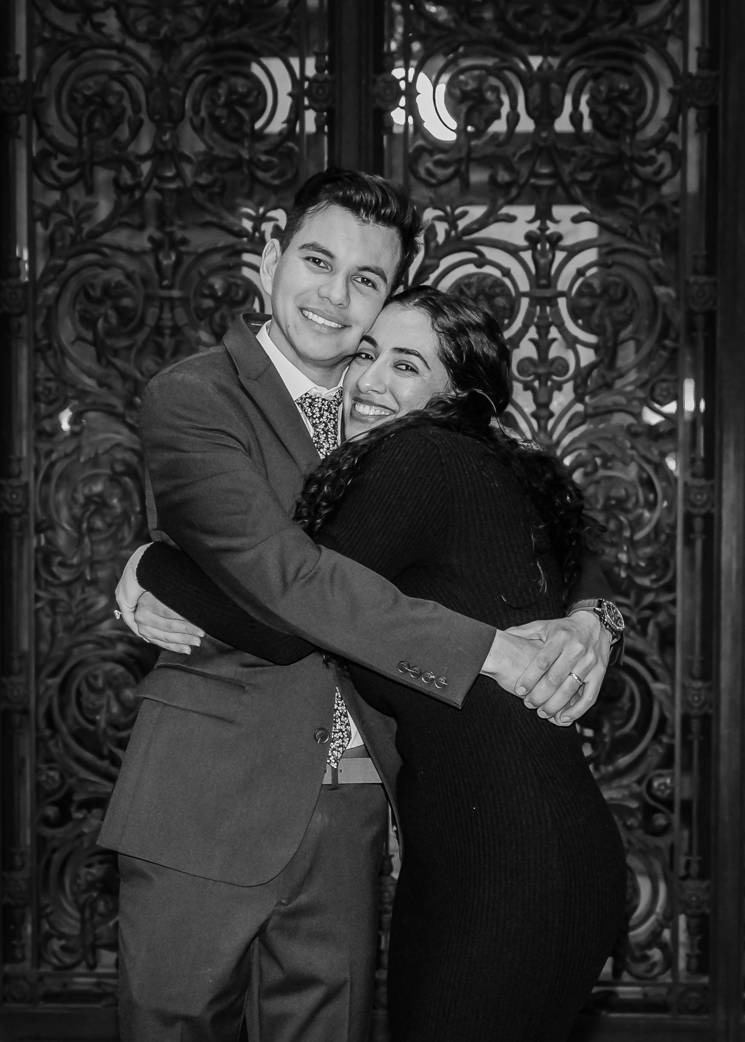 Black and white photo of groom in suit sharing a warm hug with a female guest at a wedding celebration.