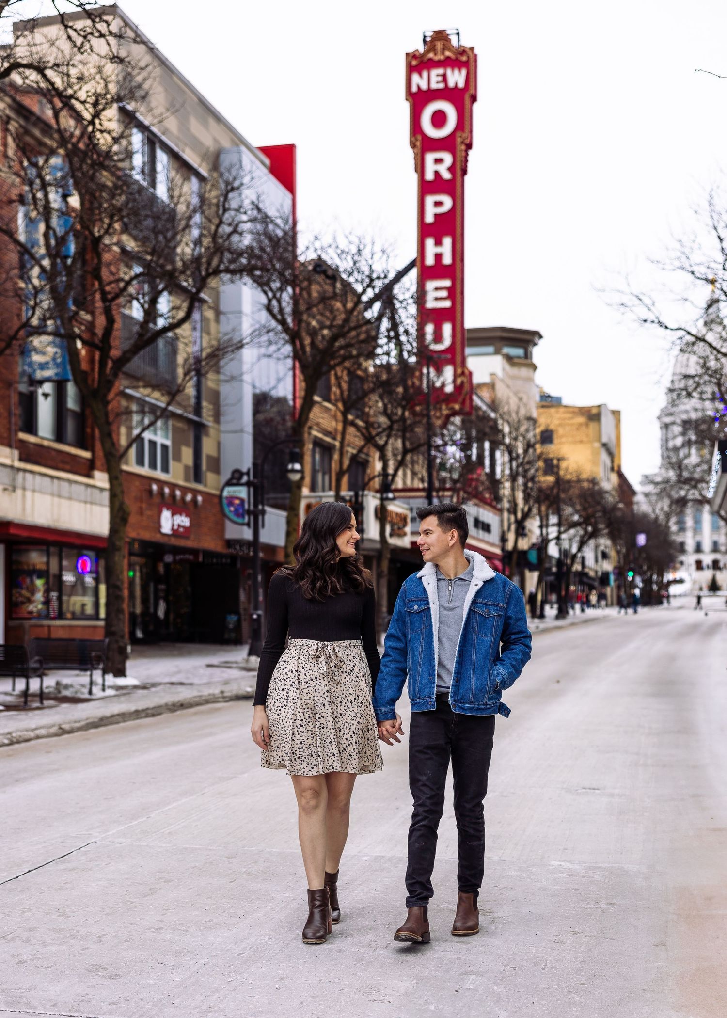 Couple walks hand in hand on a city street near the colorful New Orpheum sign.