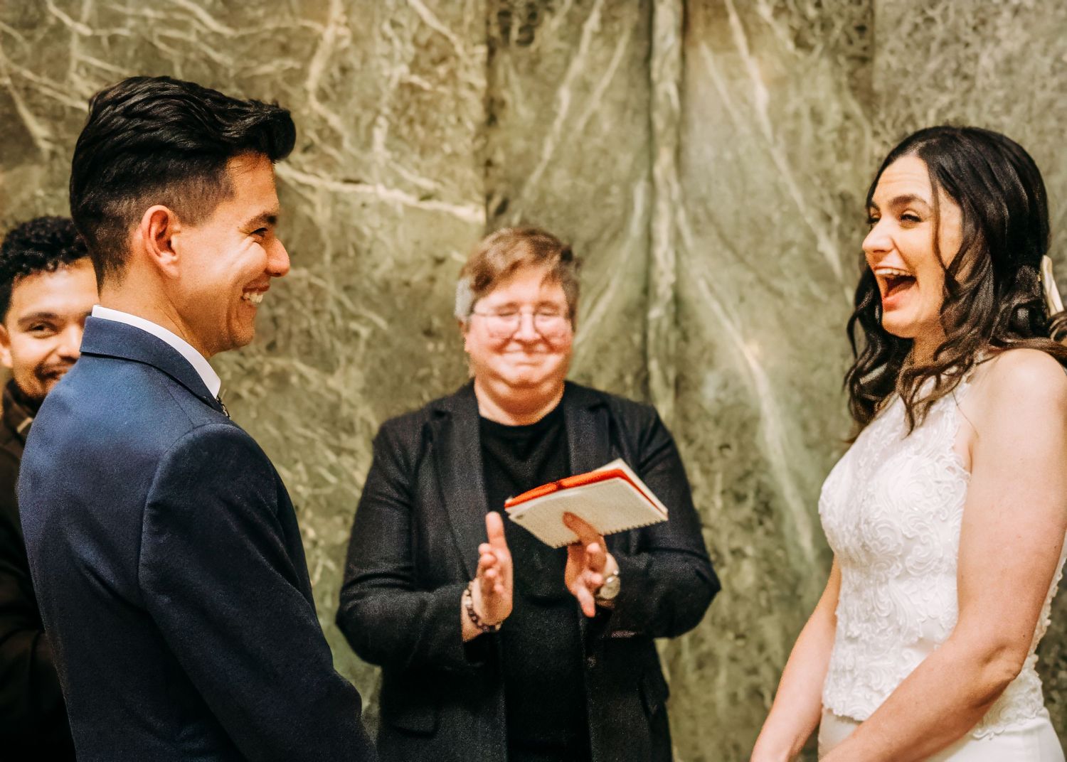 Bride and groom laughing joyfully together during wedding ceremony with applauding officiant.