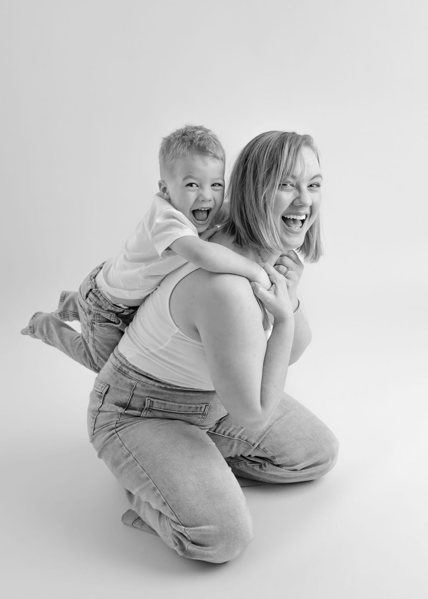 Black and white photo of laughing mother and son playing piggyback in studio portrait.