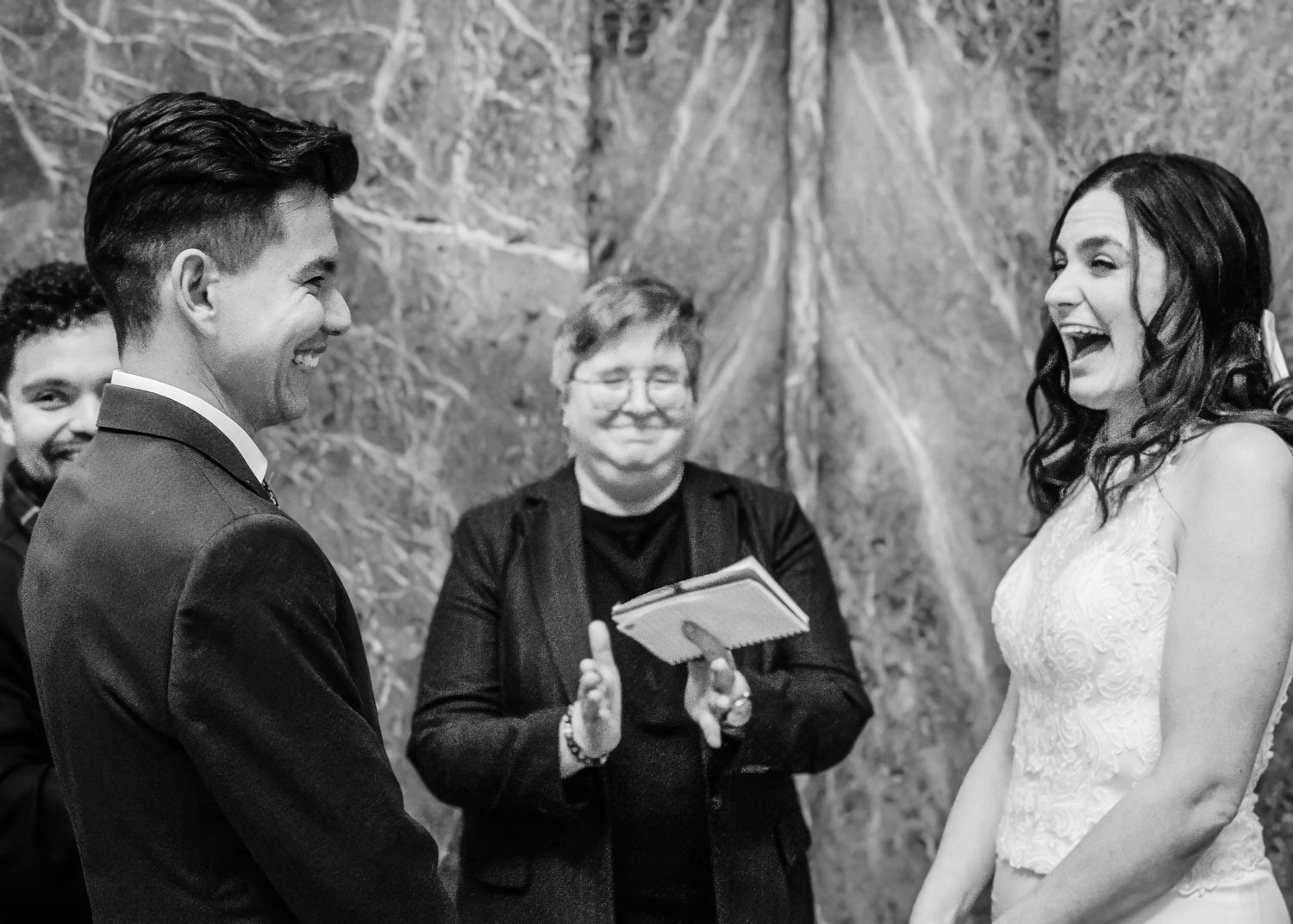 Black and white photo of laughing bride and groom during joyful wedding ceremony.