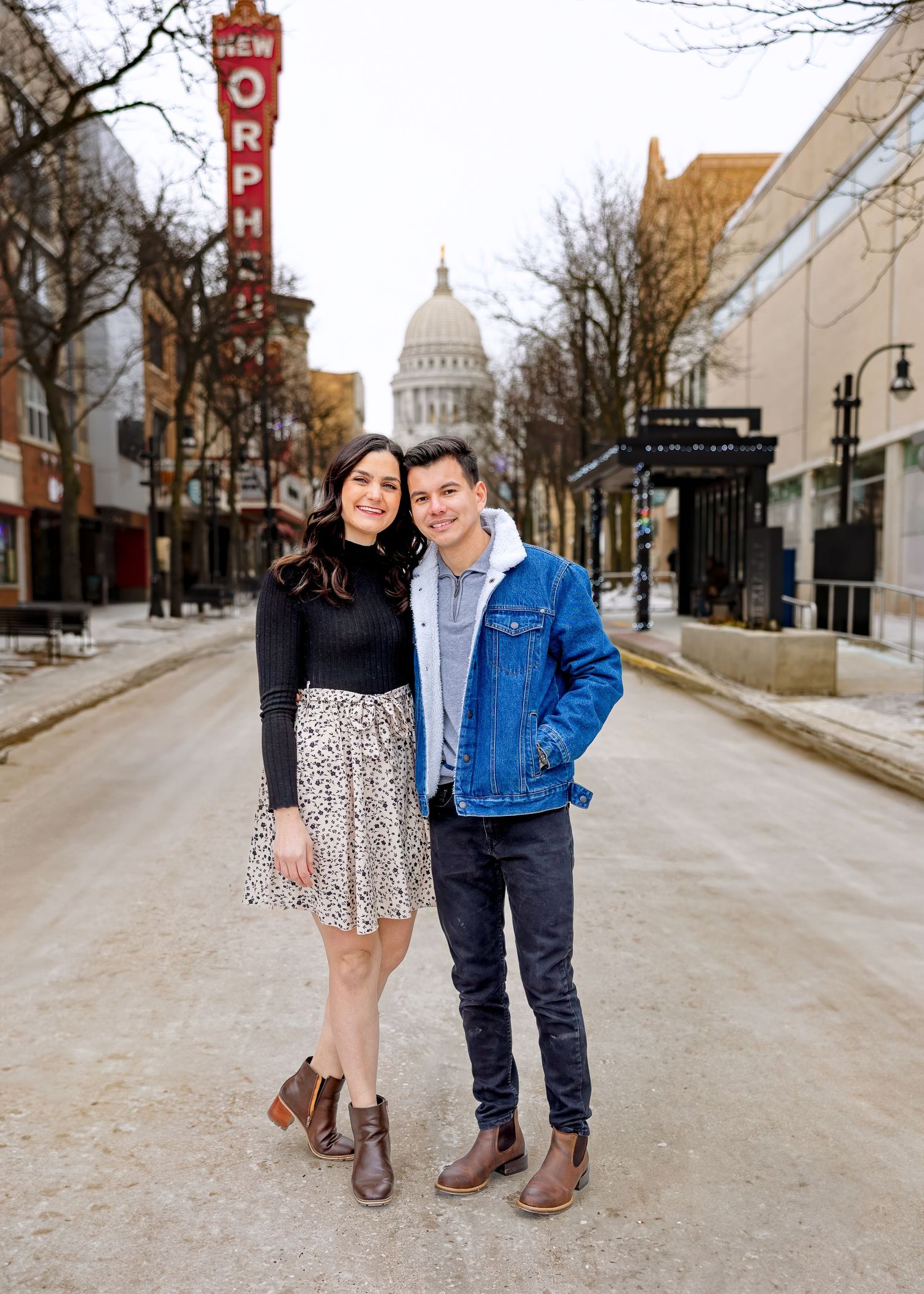 Couple posing on State Street in Madison Wisconsin with capitol building in background.